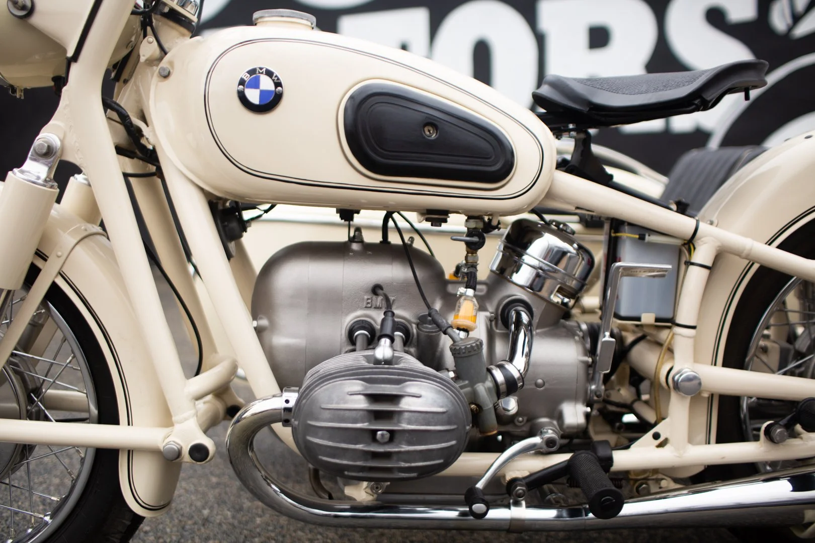 A vintage cream-colored BMW motorcycle with a black seat, chrome engine, and BMW logo on the fuel tank.