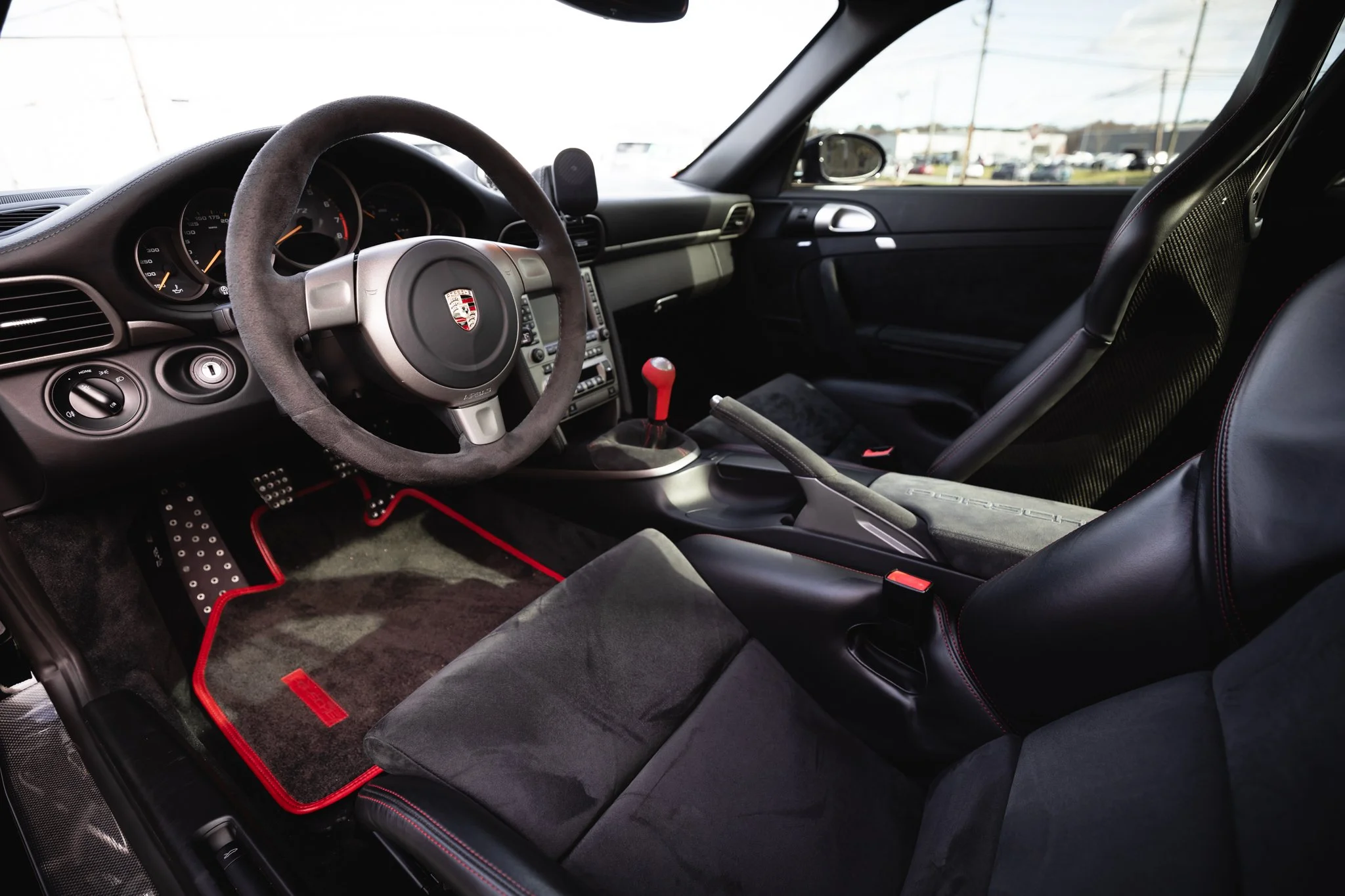 Interior of a sports car, showing a racing steering wheel, gear shift, and racing seats with red stitching.