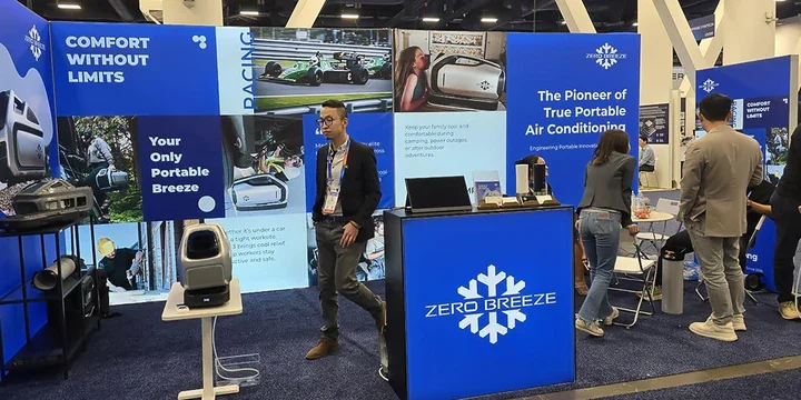 Trade show booth for Zero Breeze featuring promotional banners for portable air conditioning units, with representatives and attendees interacting.