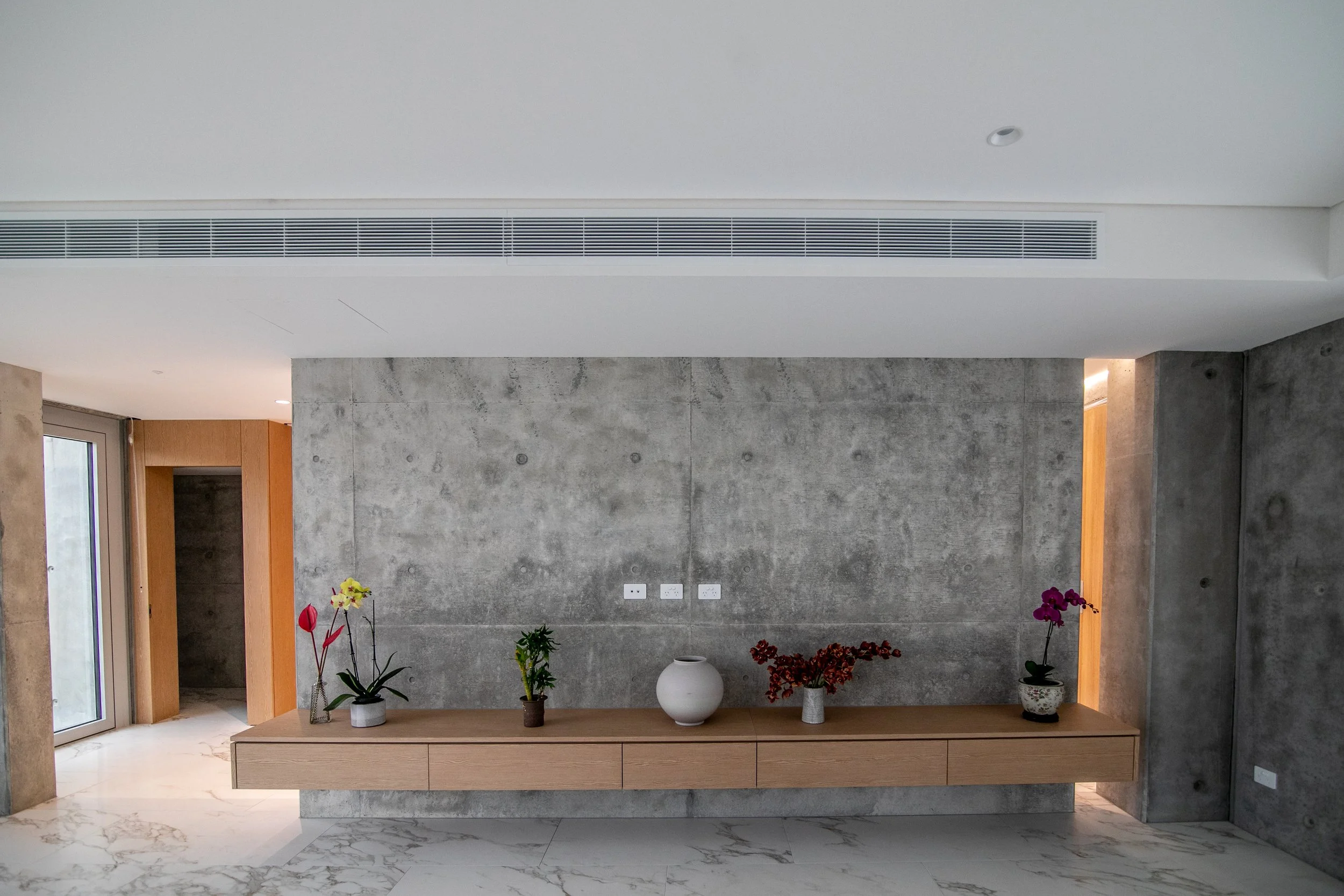 Off-form concrete interior wall with floating timber cabinetry inside the Balwyn North concrete house.