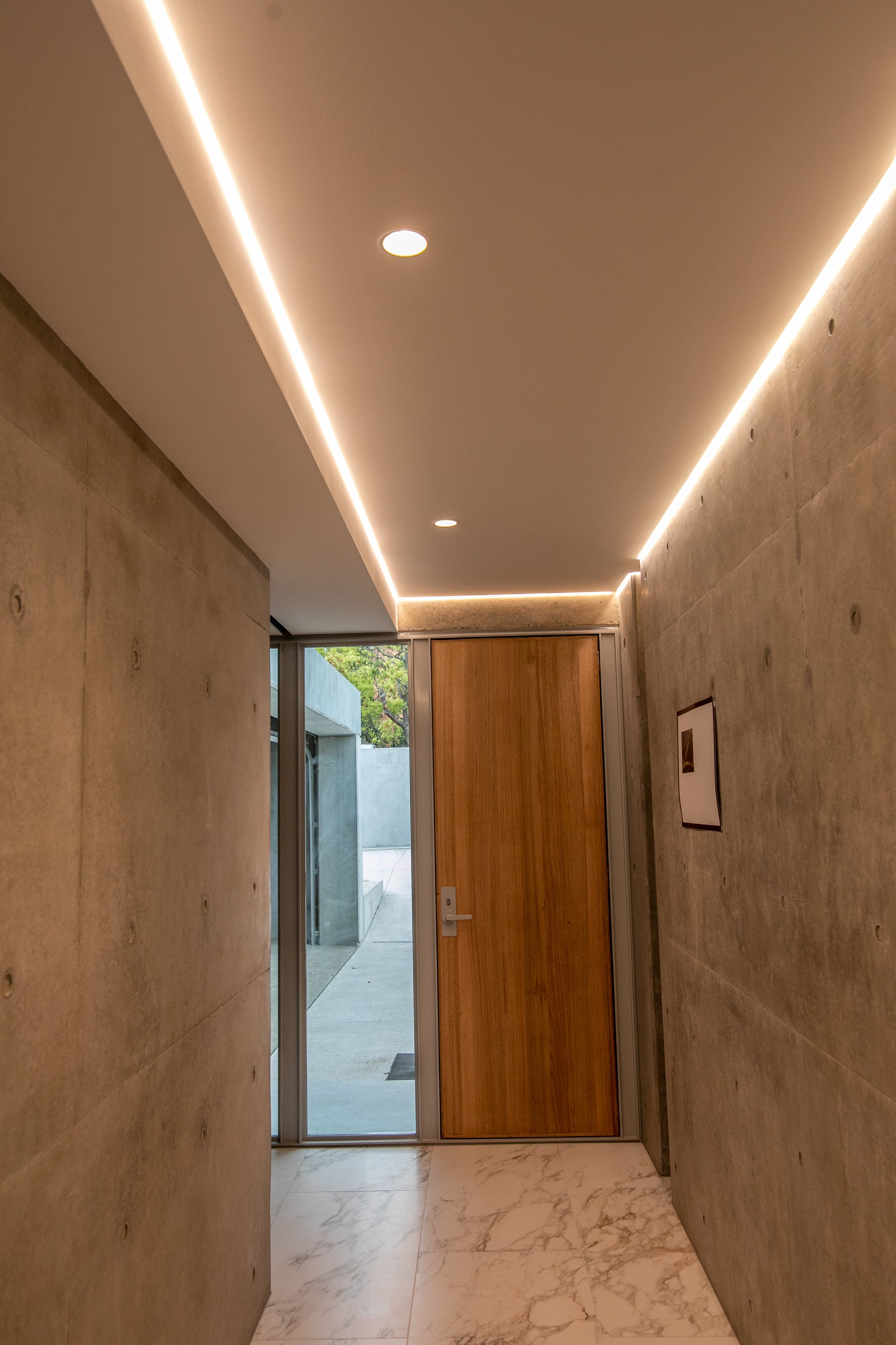 Concrete entrance corridor with a timber door and integrated linear lighting in a Balwyn North home.