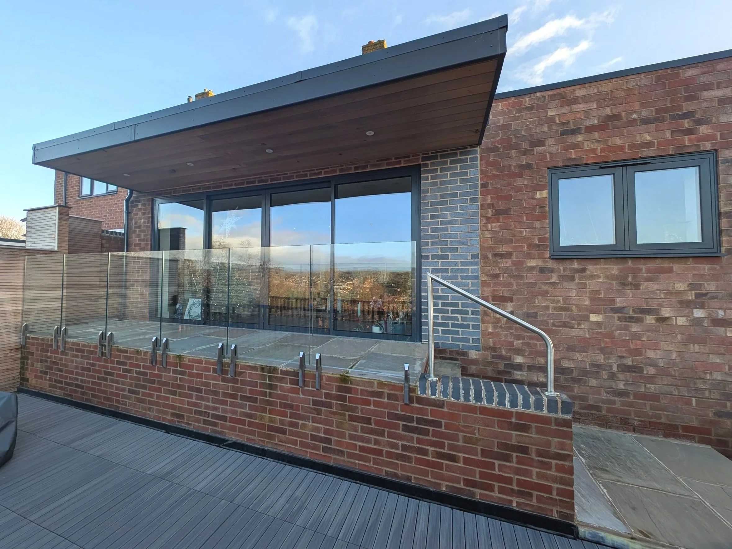 The completed terrace at Peak View, featuring the newly installed glass balustrades between the upper patio and lower timber deck, with the Peak District hills reflected.