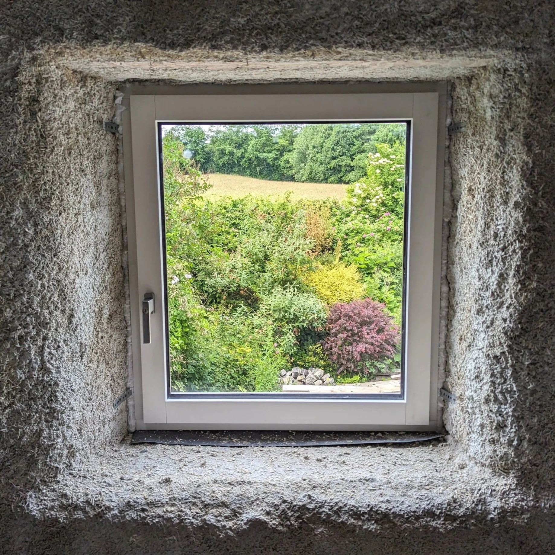 High-performance triple-glazed window frame set directly within a 150mm breathable natural hemp-lime insulation structure, photographed during the heritage deep retrofit phase at Owlet House