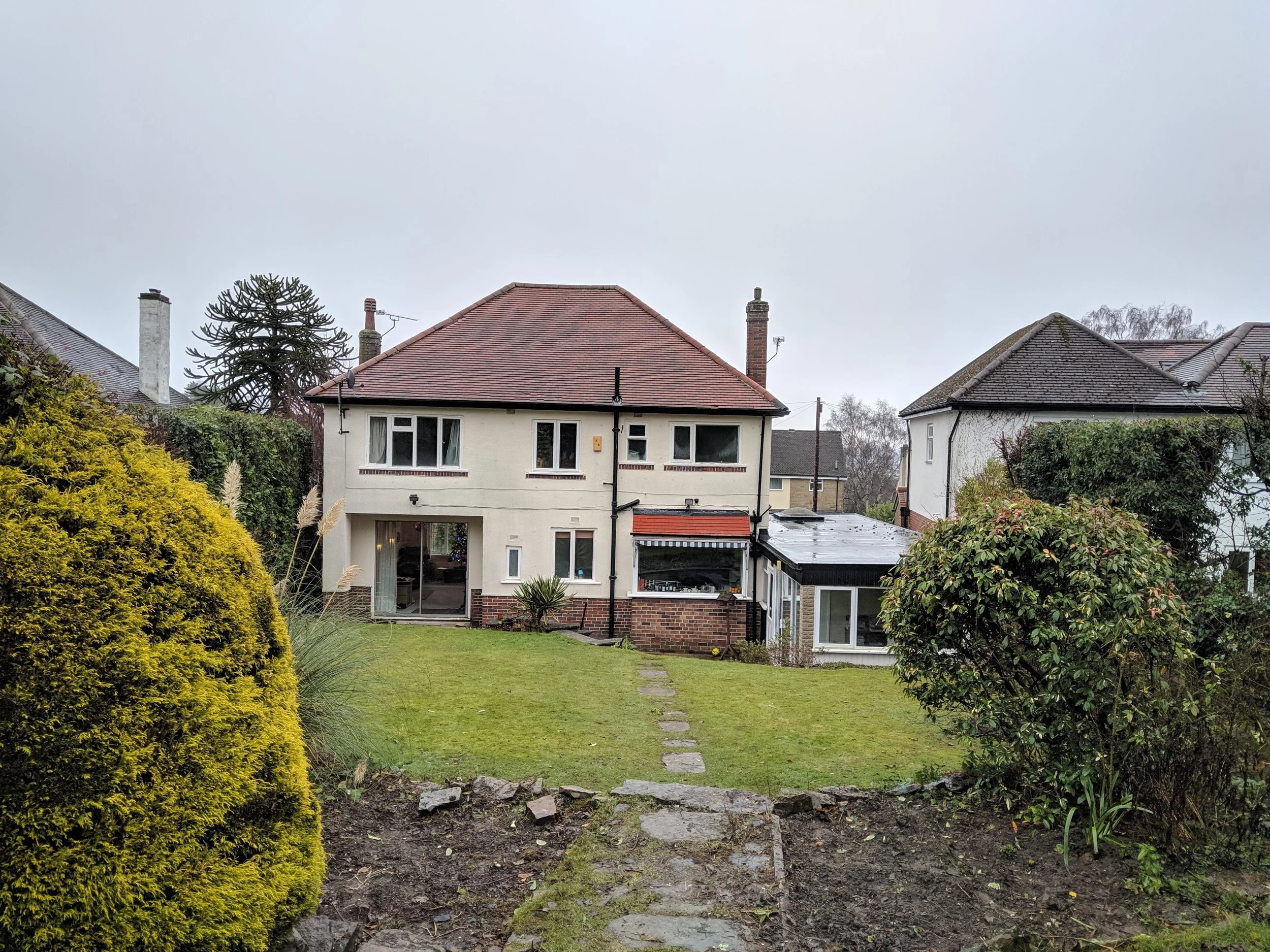 Rear exterior of the original 1930s house in Sheffield showing the outdated 1970s glazed conservatory prior to demolition.