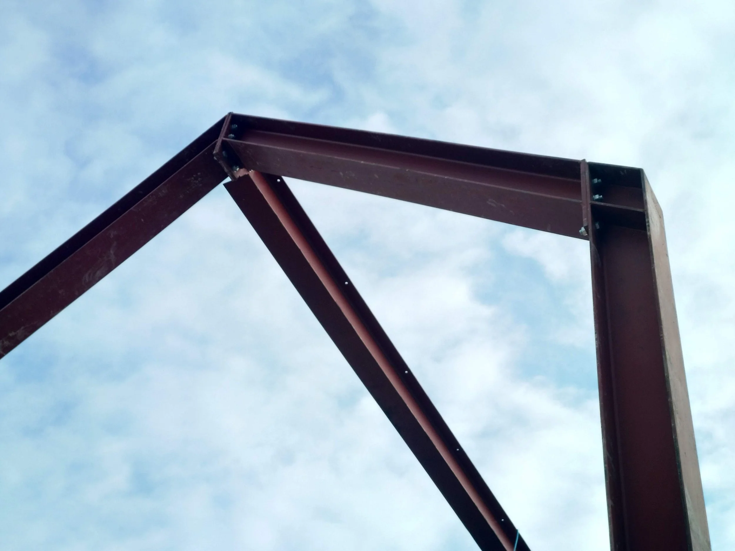 Erection of structural red steel apex portal frame against the sky during double-height rear extension construction in Sheffield.