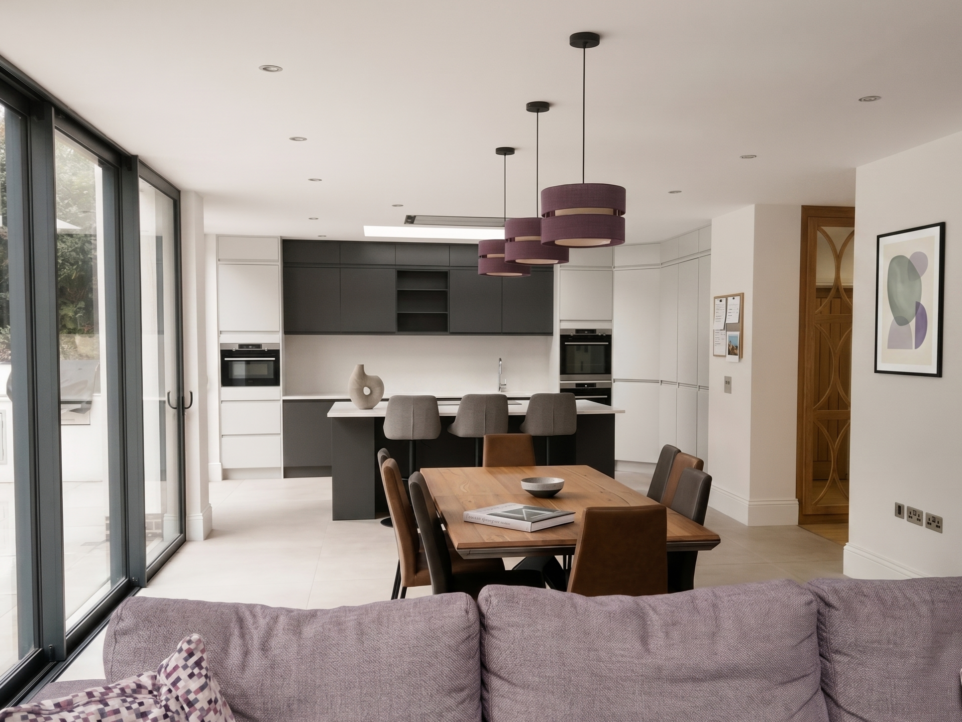Bright open-plan kitchen, dining, and family living area with neutral tiling, modern cabinetry, and bifold doors opening to the patio.