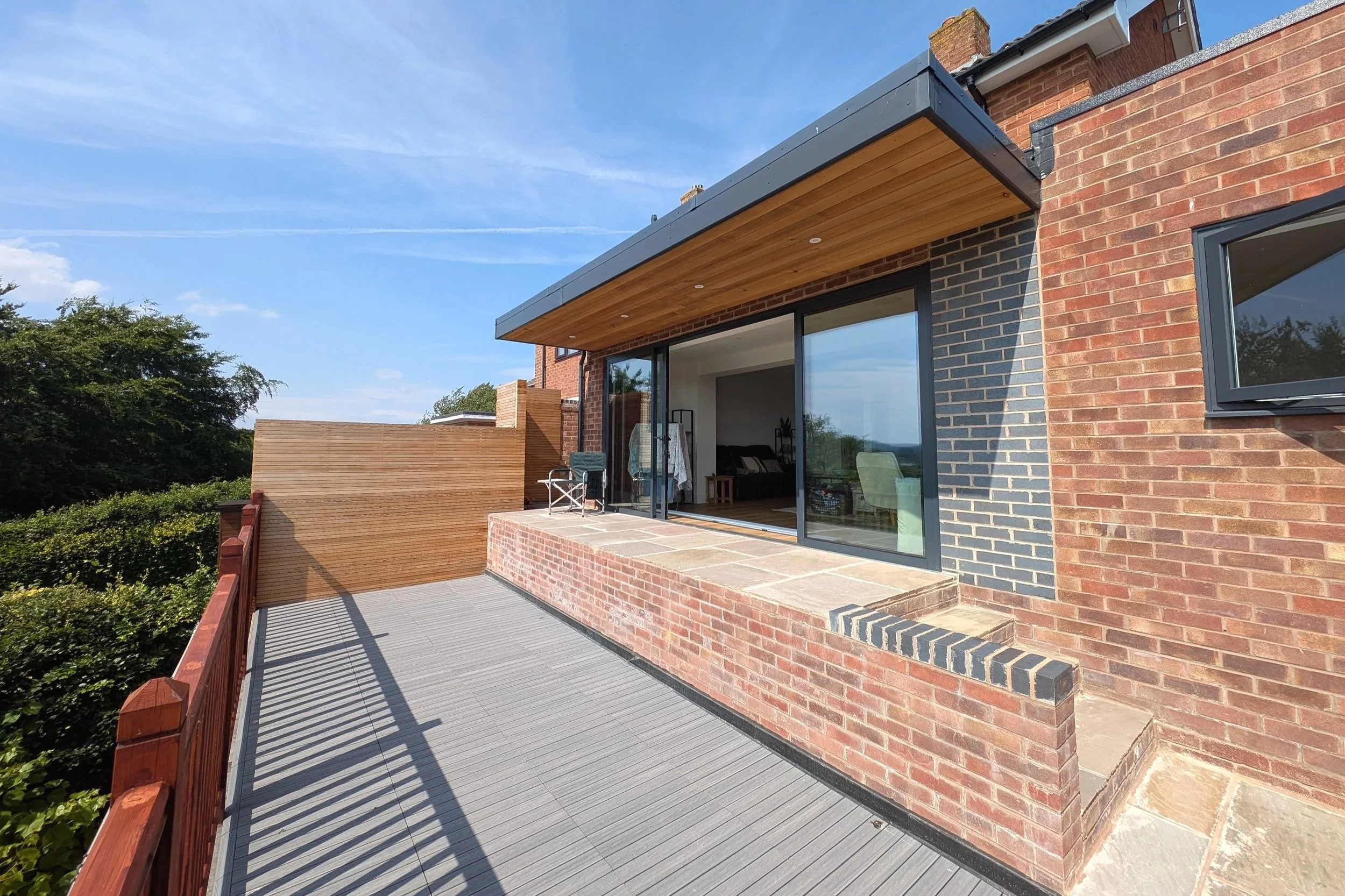 View looking across the upper terrace paving, which sits flush with the sliding door thresholds for level access, leading down to the new timber decking on the lower garden store roof.