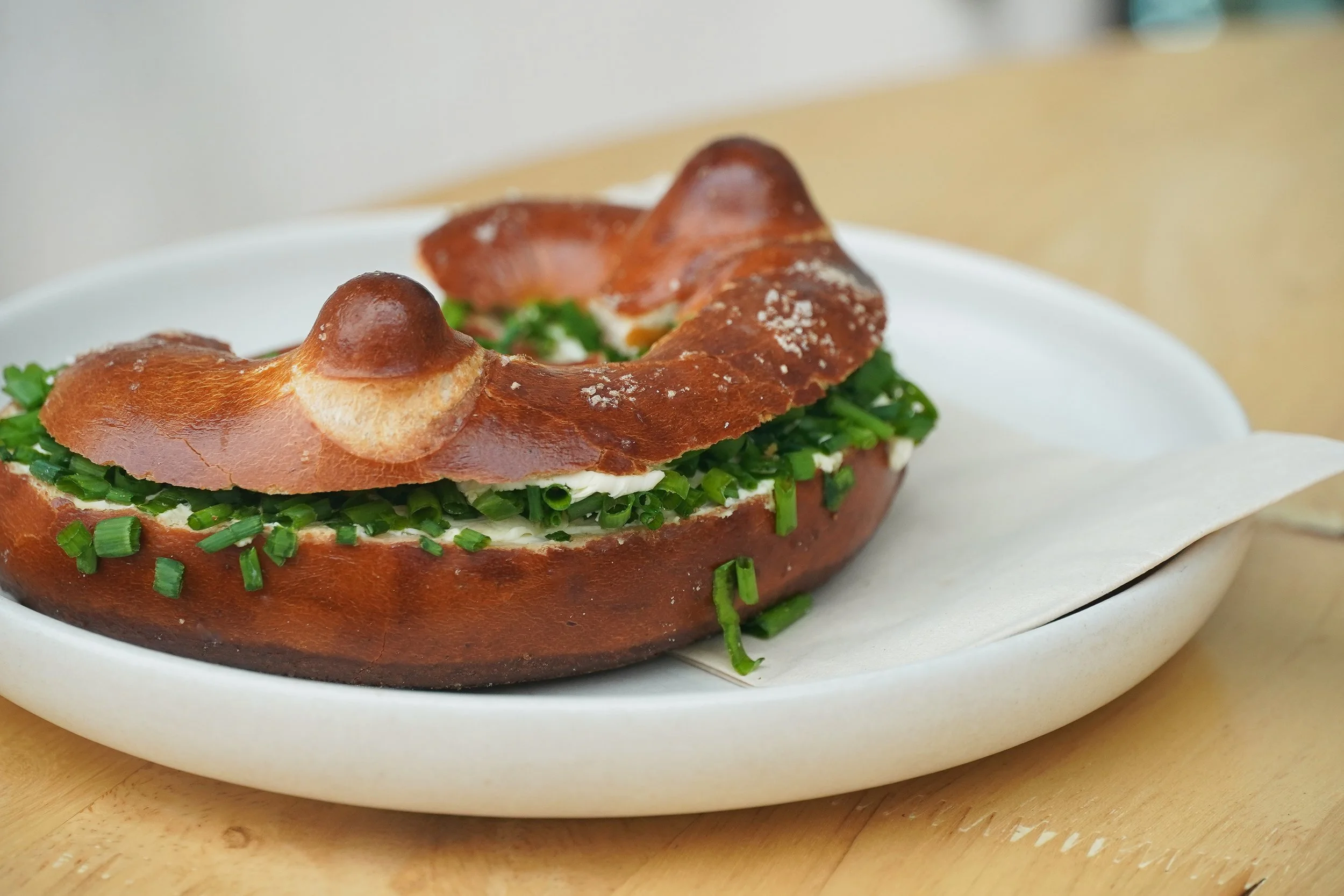 Baked bread bowl filled with chopped green onions and cream, topped with a brown roasted bread cap, on a white plate.