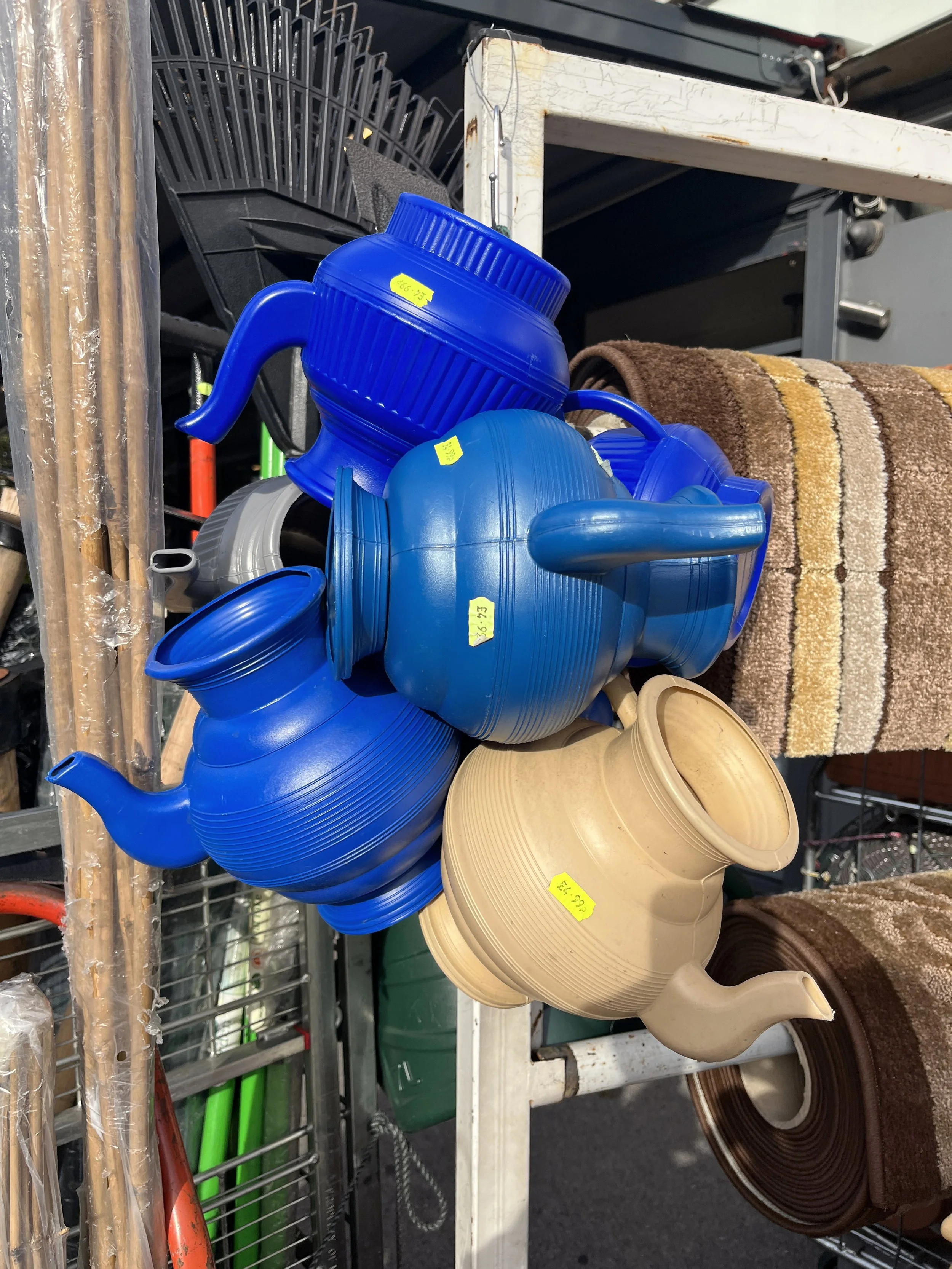 A pile of blue and beige plastic teapots and kettles displayed on a metal rack at a store.