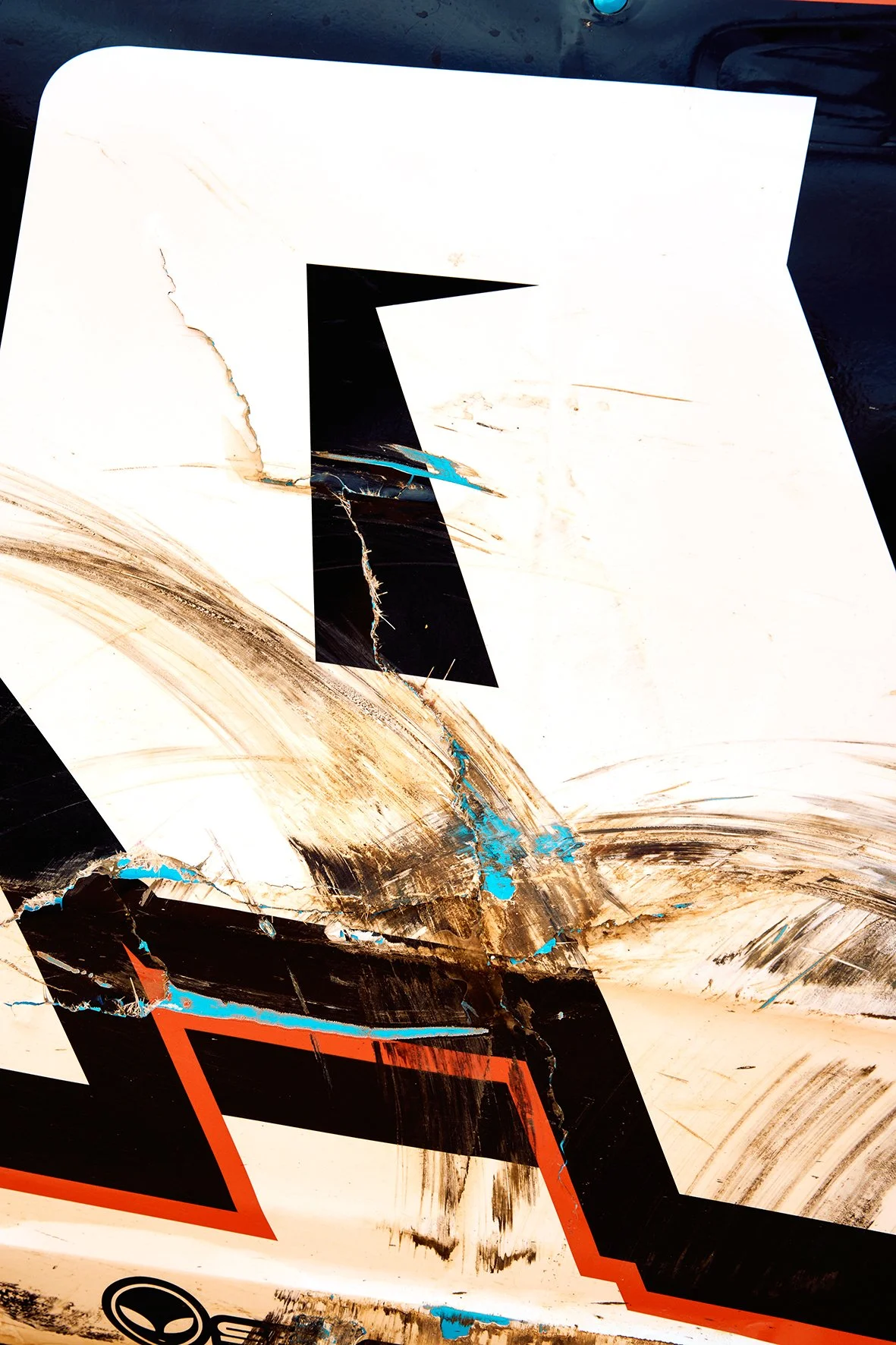 A damaged race car with black, white, blue, and red designs, showing scratches, cracks, and dirt.