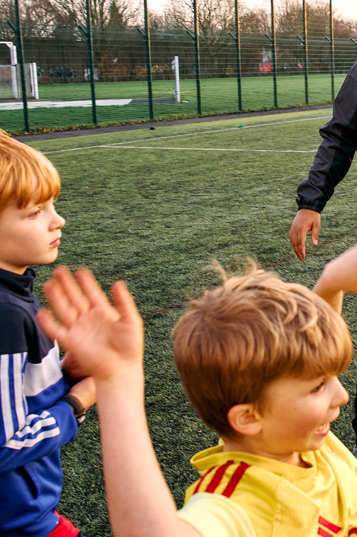 Children on a soccer field with a person in black jacket.