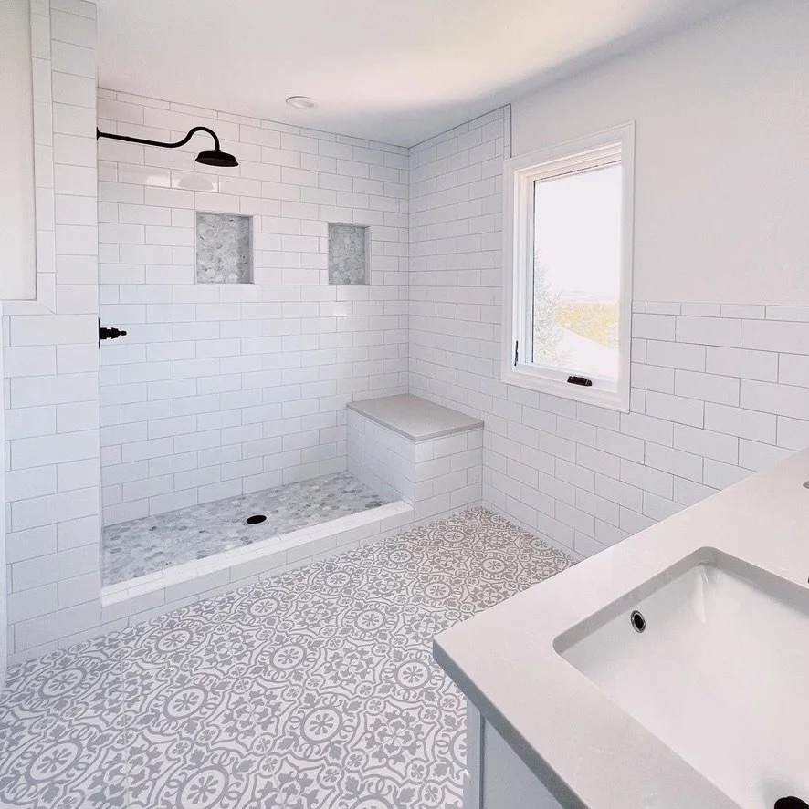 White modern bathroom with subway tiles, a walk-in shower featuring built-in shelves, patterned floor tiles, and a double sink vanity.