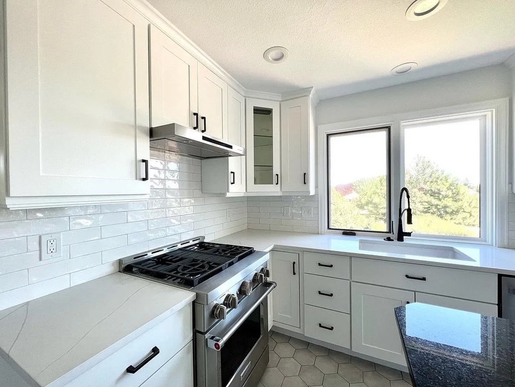 Modern kitchen with white cabinets, stainless steel gas stove, subway tile backsplash, and a large window above the sink.