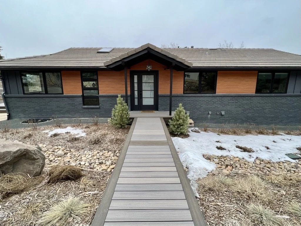 Modern single-story house with a wooden walkway, flat roof, and minimalist landscaping.