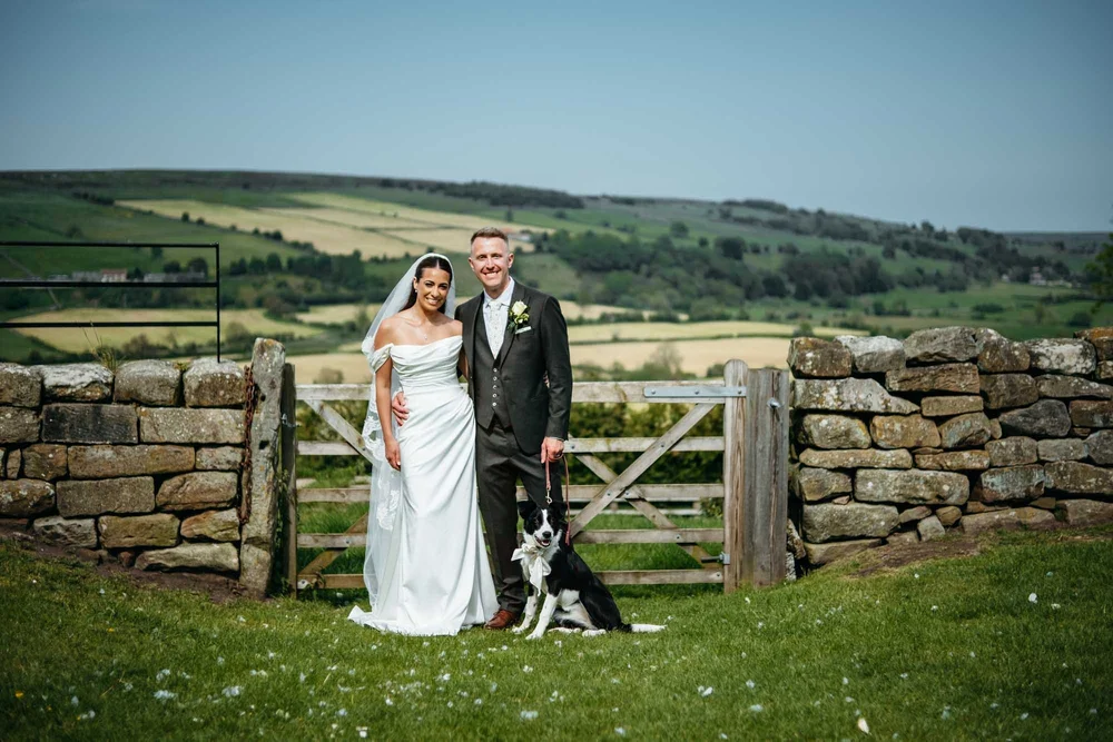 Bride and groom with their border collie at the gate at Danby Castle after their wedding ceremony