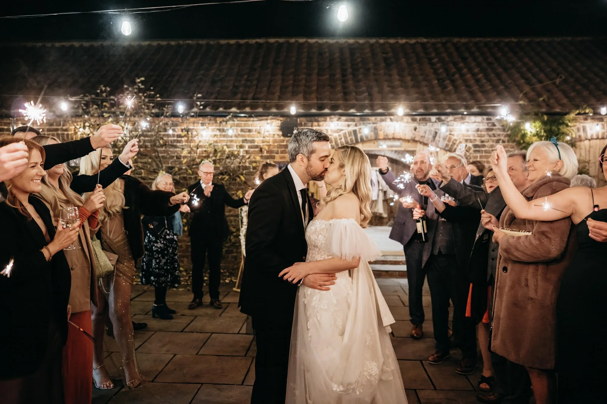 Couple kissing at night as guests wave sparklers around them
