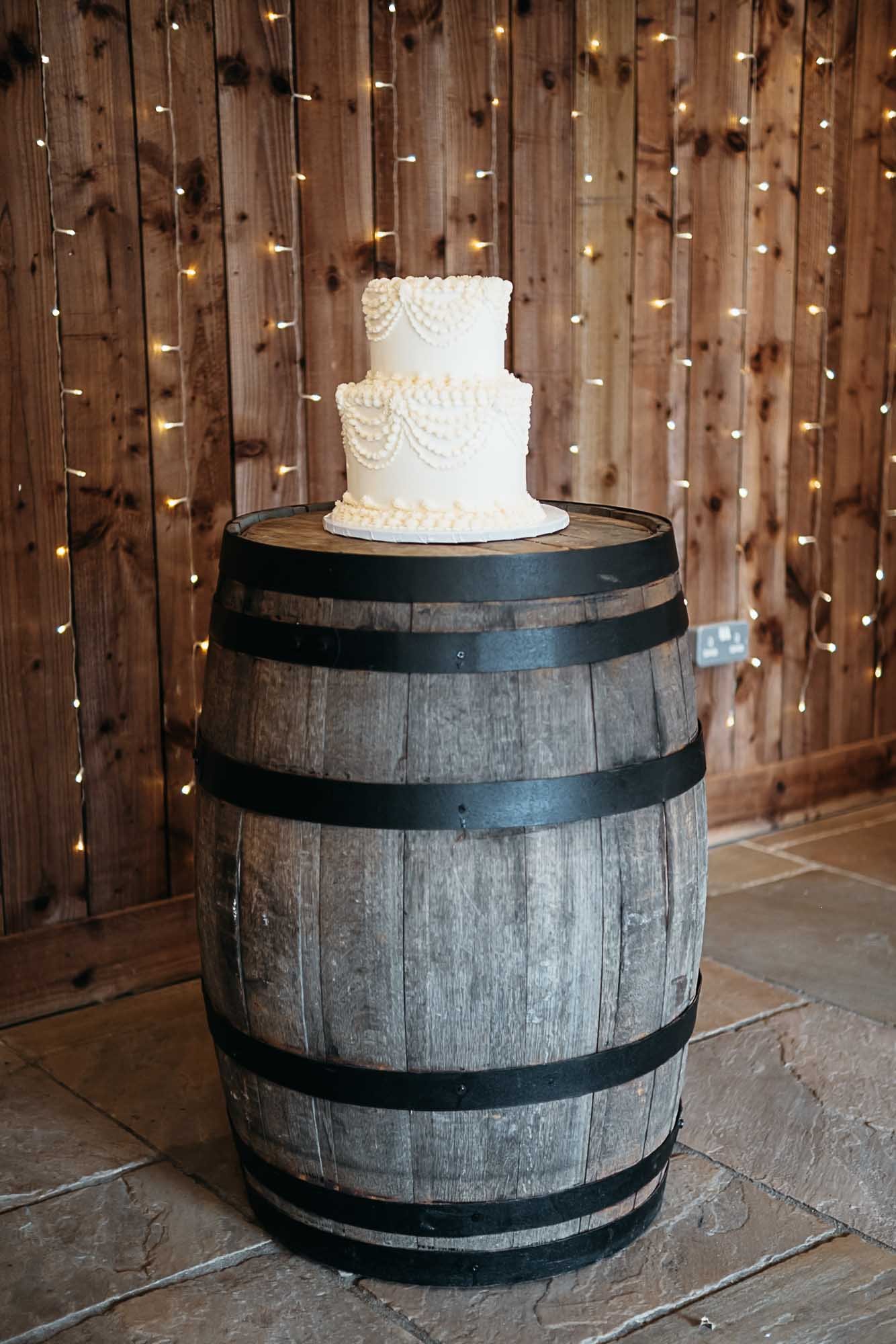 The wedding cake on a wooden barrel against a timber wall