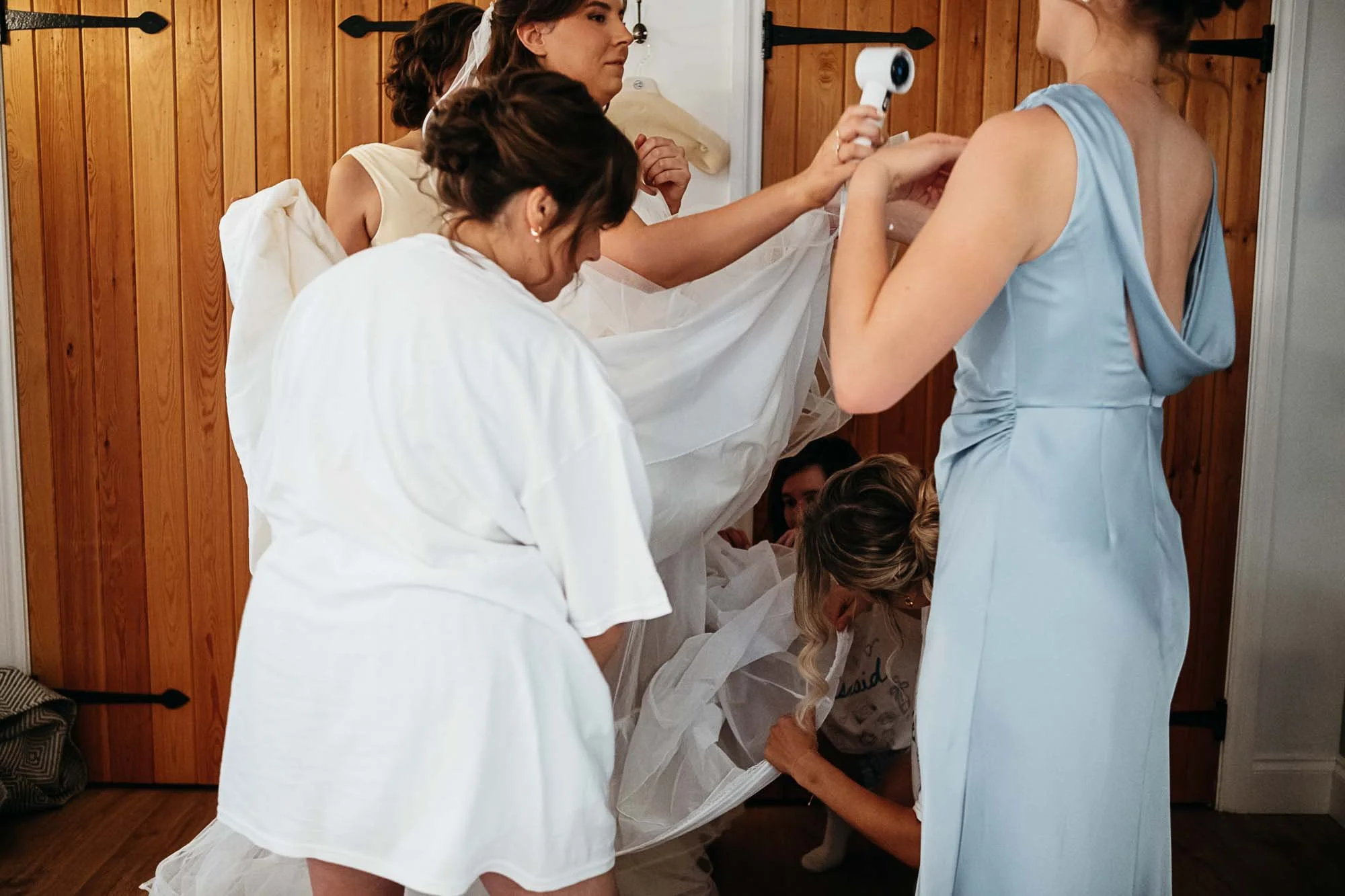 Aimee's dress being laced up by a bridesmaid in a blue dress