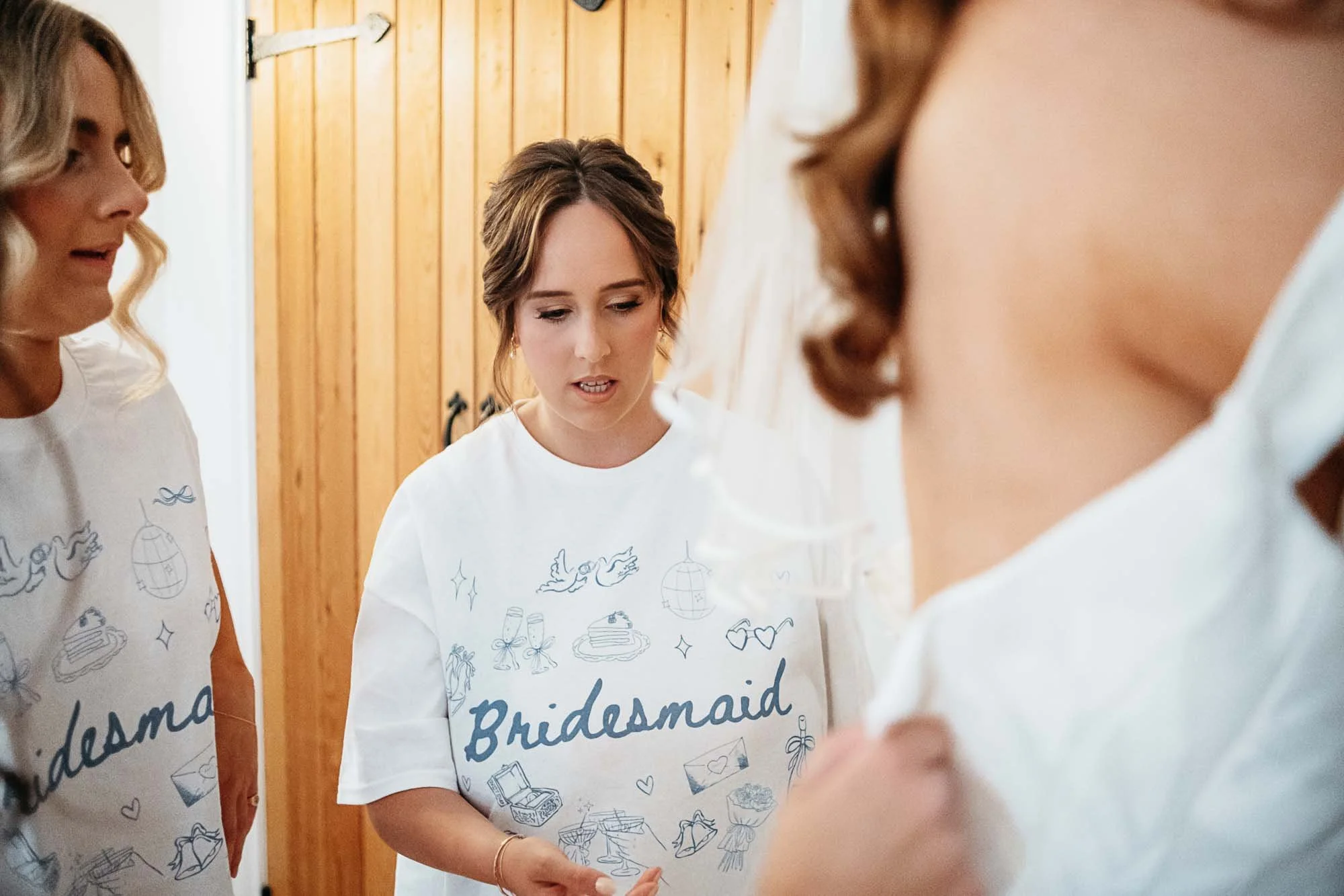 A bridesmaid in a Bridesmaid T-shirt helping with Aimee's dress