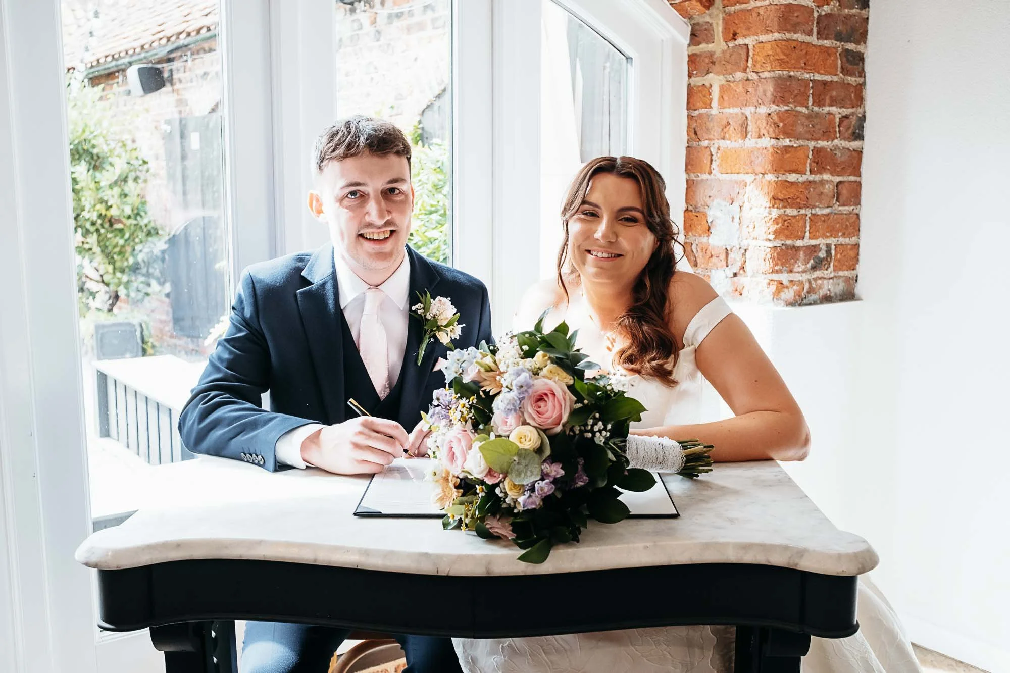 Aimee and Dan signing the register at a table with a pastel bouquet