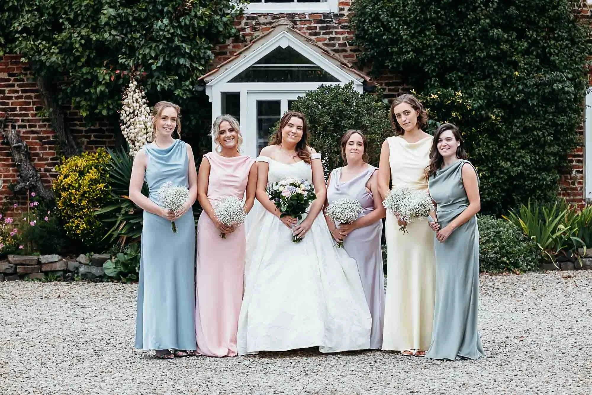 Aimee with her bridesmaids, each in a different pastel dress, in the gardens