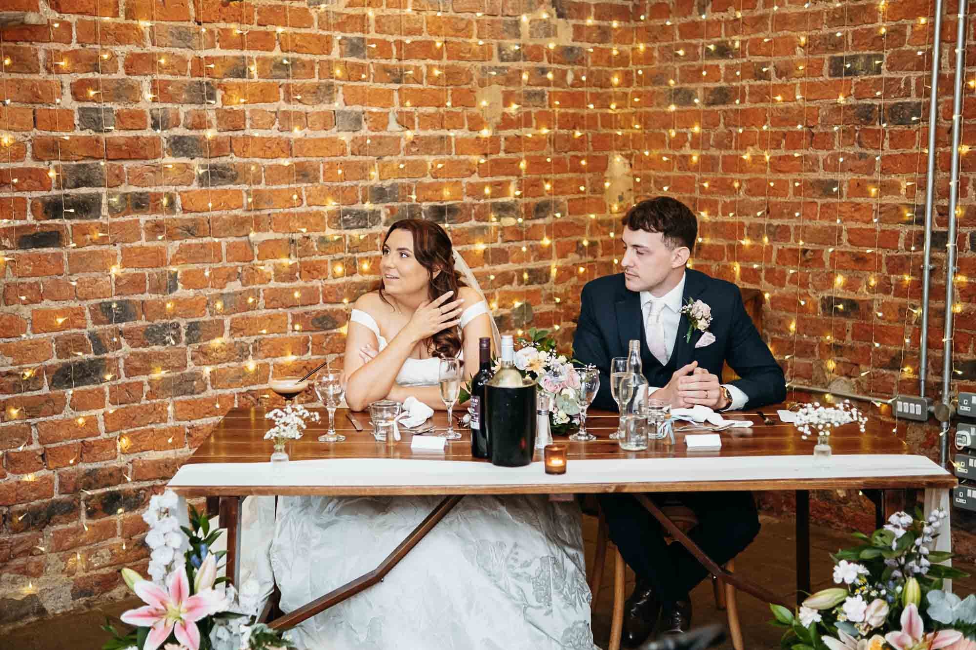 Aimee and Dan at their table against the brick wall during the wedding breakfast