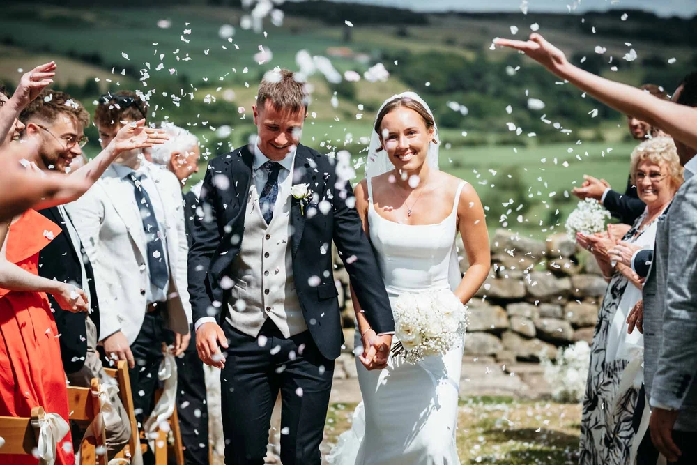 Bride and groom walking through confetti thrown by guests at Danby Castle