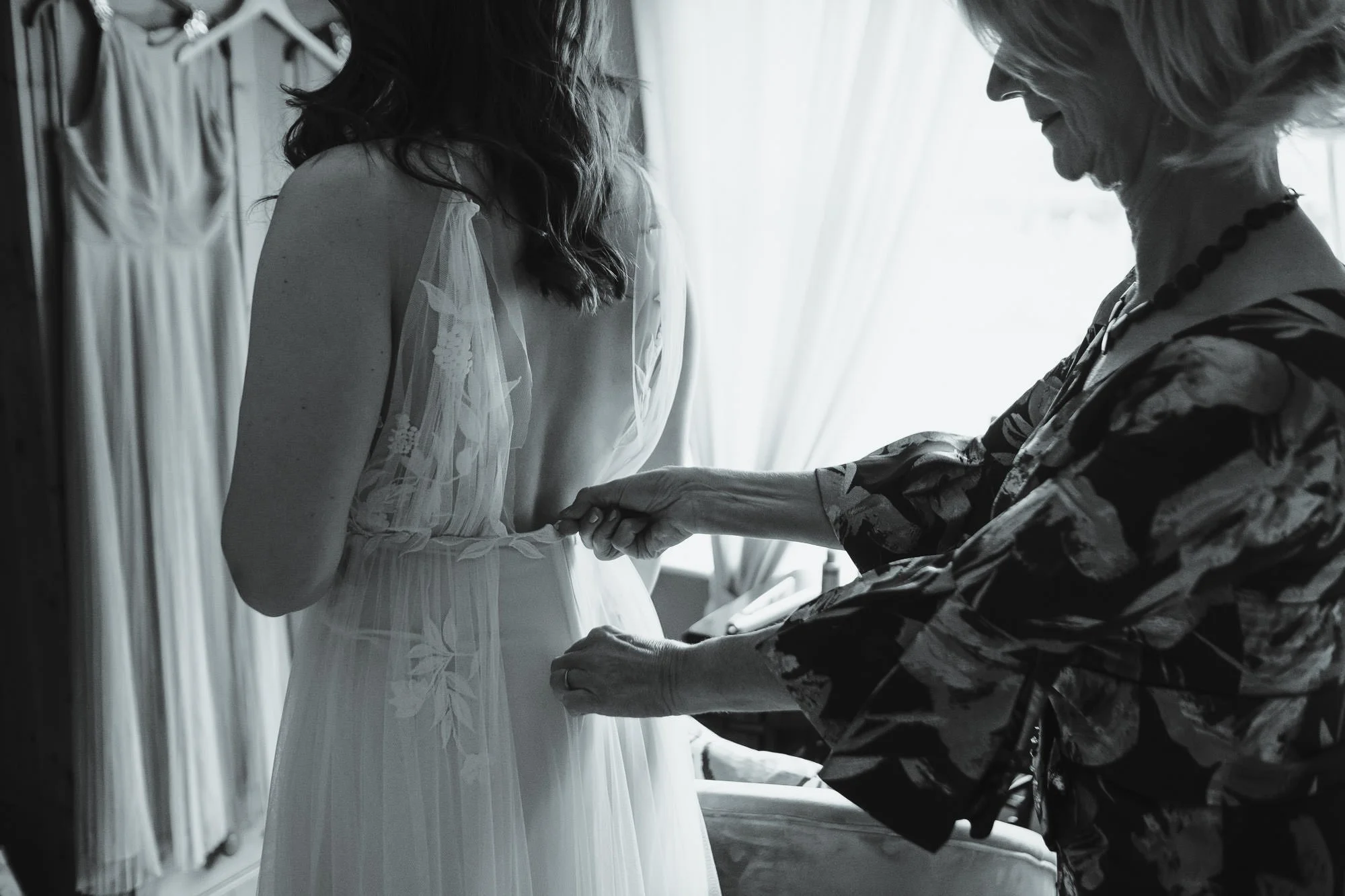 A woman helping a bride with her wedding dress in a softly lit room.
