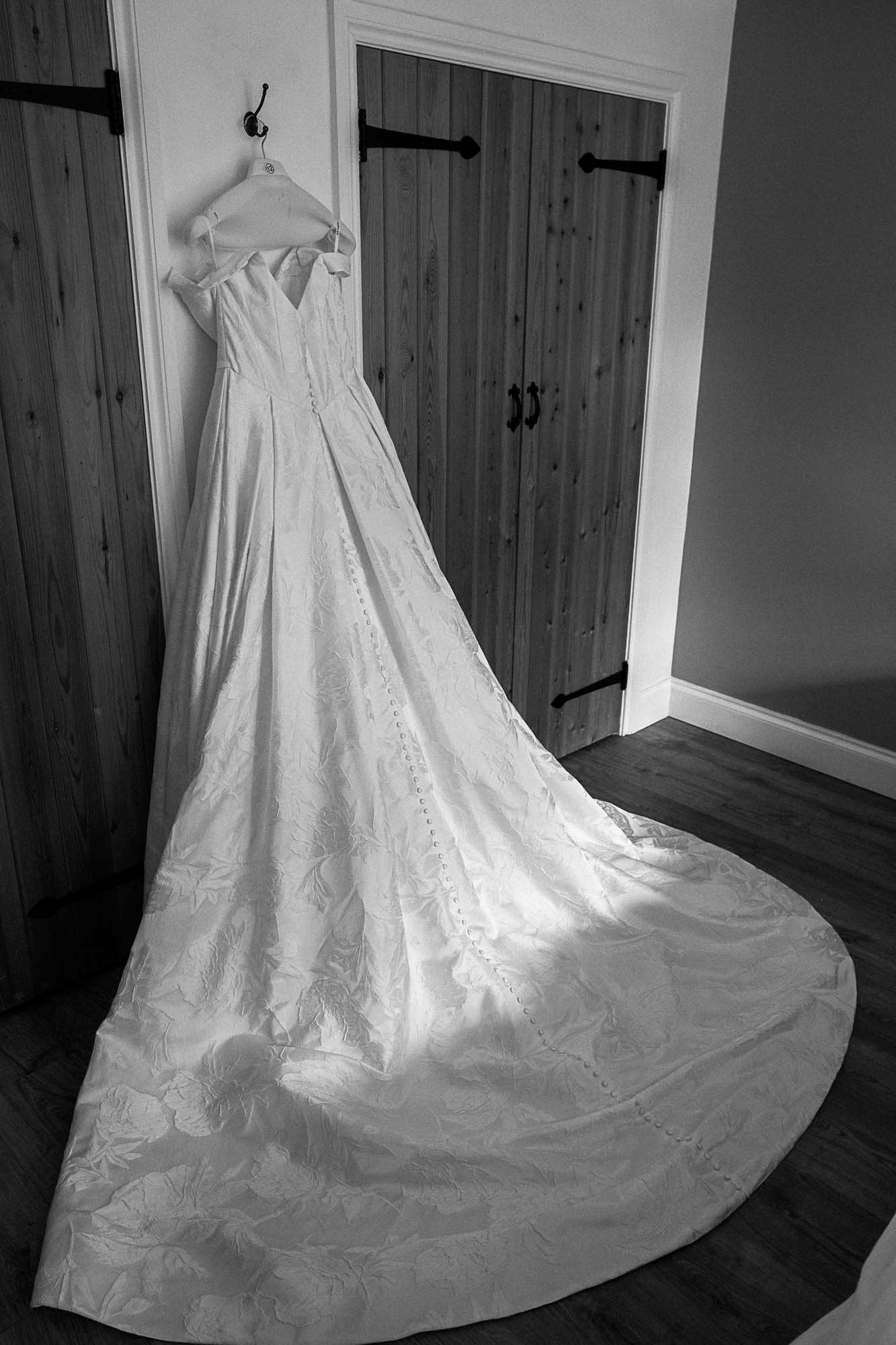 Aimee's wedding dress hanging by a wooden door, its long train spread across the floor
