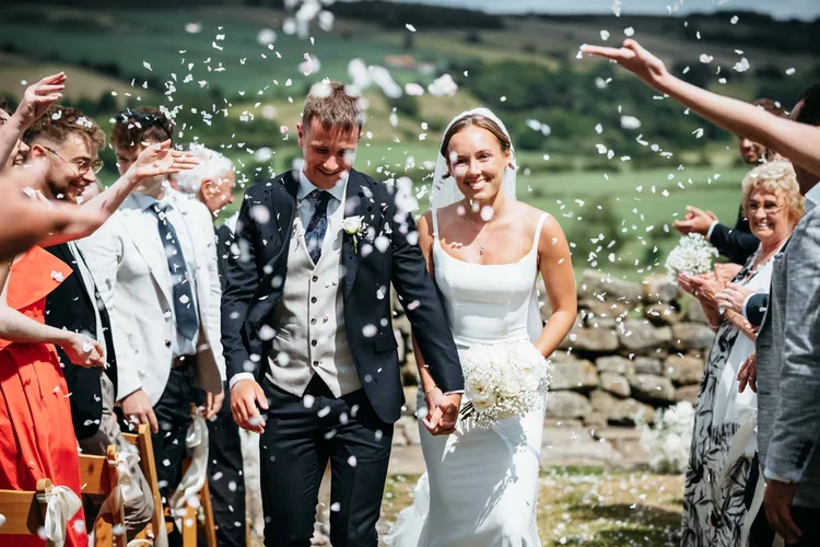 Bride and groom walking through confetti thrown by guests at Danby Castle