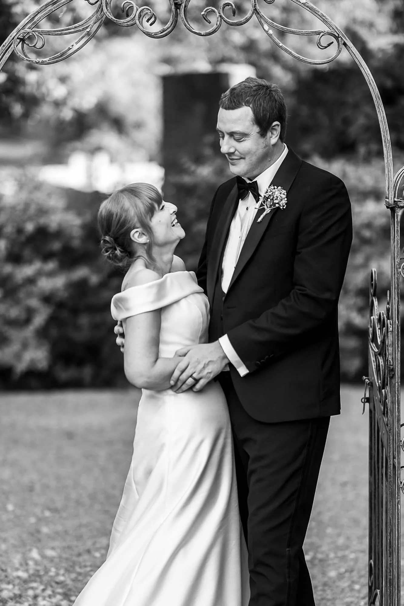 Black and white photograph of a bride laughing with her groom beneath the iron garden arch at The Croft Hotel
