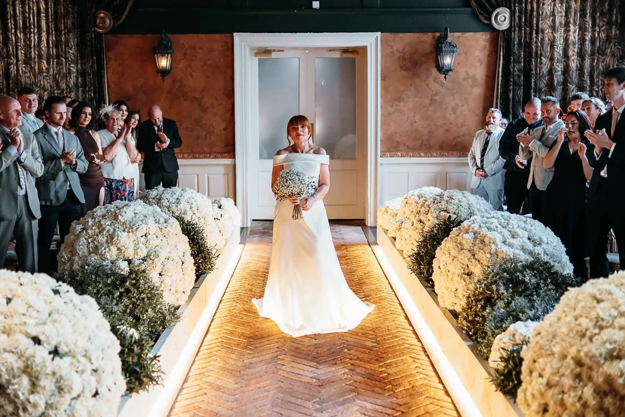 Bride walking the lit runway aisle in the Secret Garden Chapel at The Croft Hotel as guests stand either side