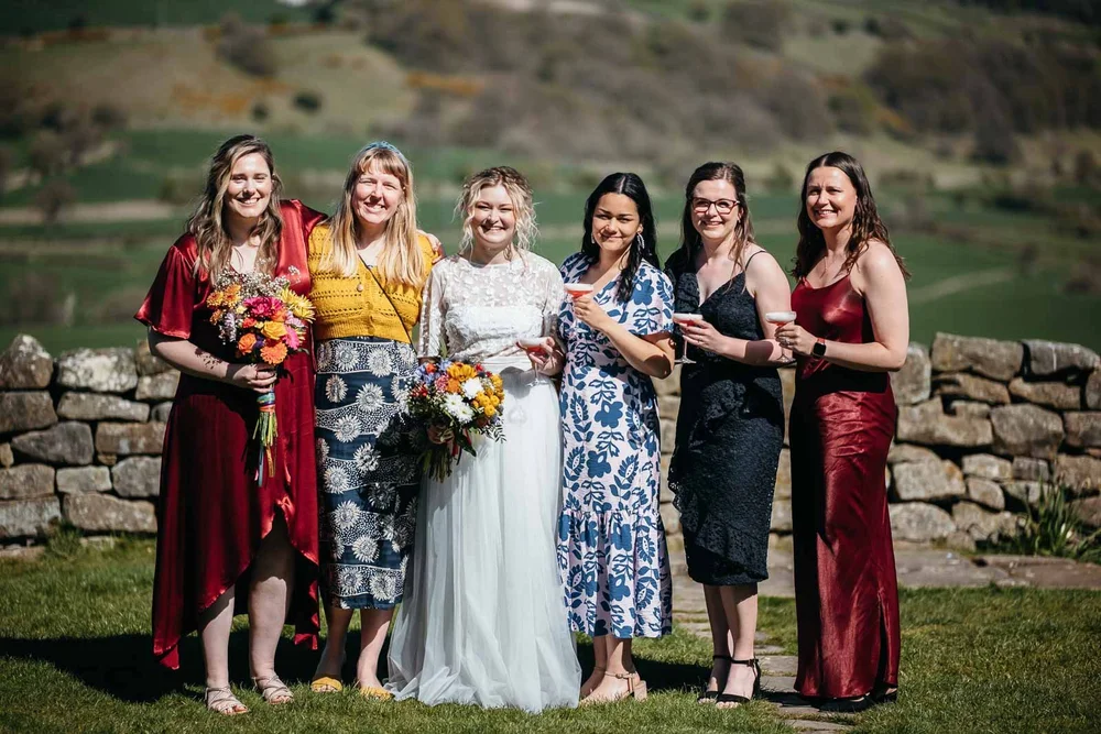 Bride with friends beside the dry stone wall at Danby Castle with the Esk Valley behind them
