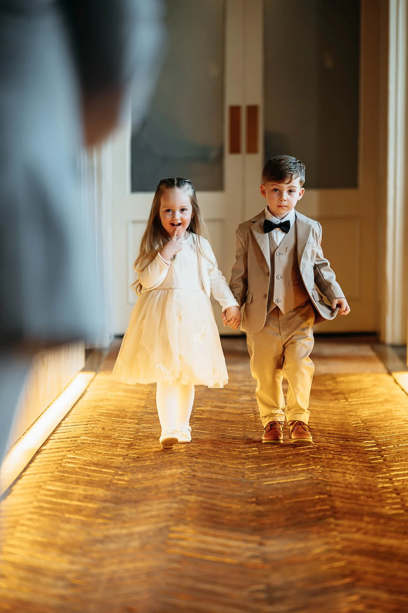 A flower girl and page boy walking hand in hand down the uplit aisle at The Croft Hotel