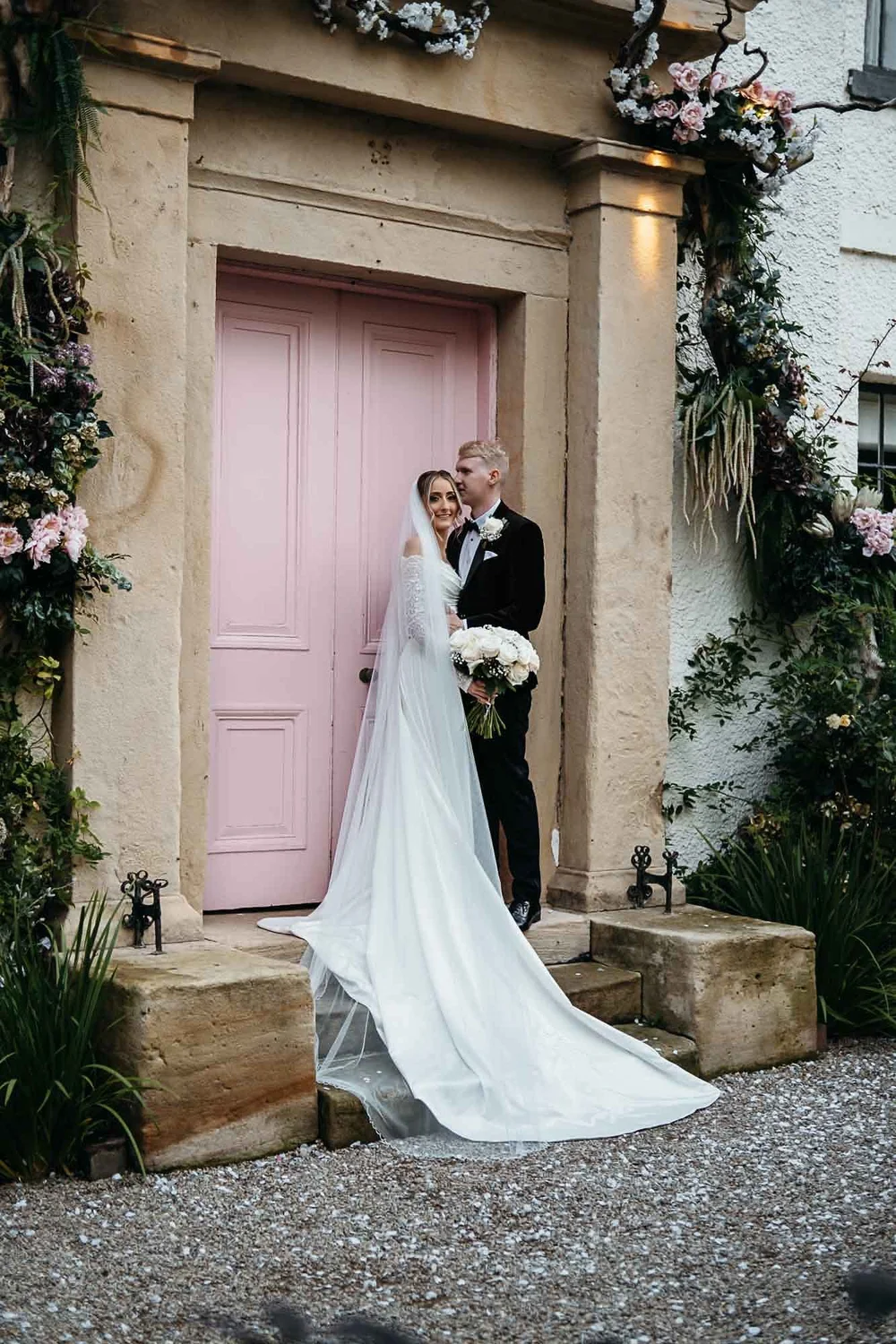 Bride and groom at the pink door at The Croft Hotel framed by pink blossom styling
