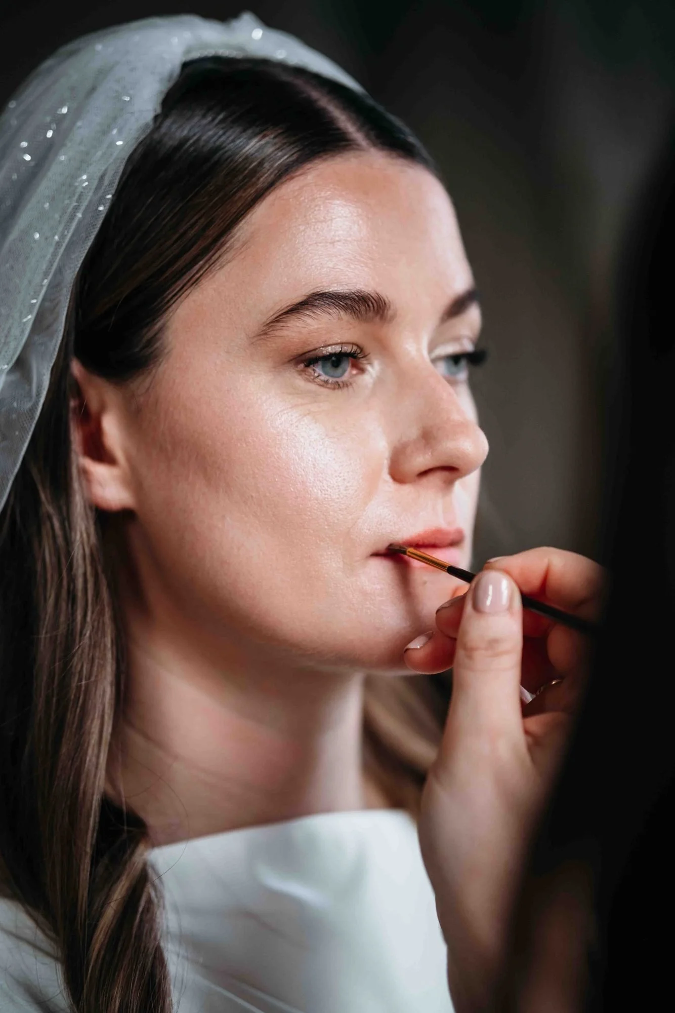 Bride putting on her lipstick, veil in her hair, at Middleton Lodge