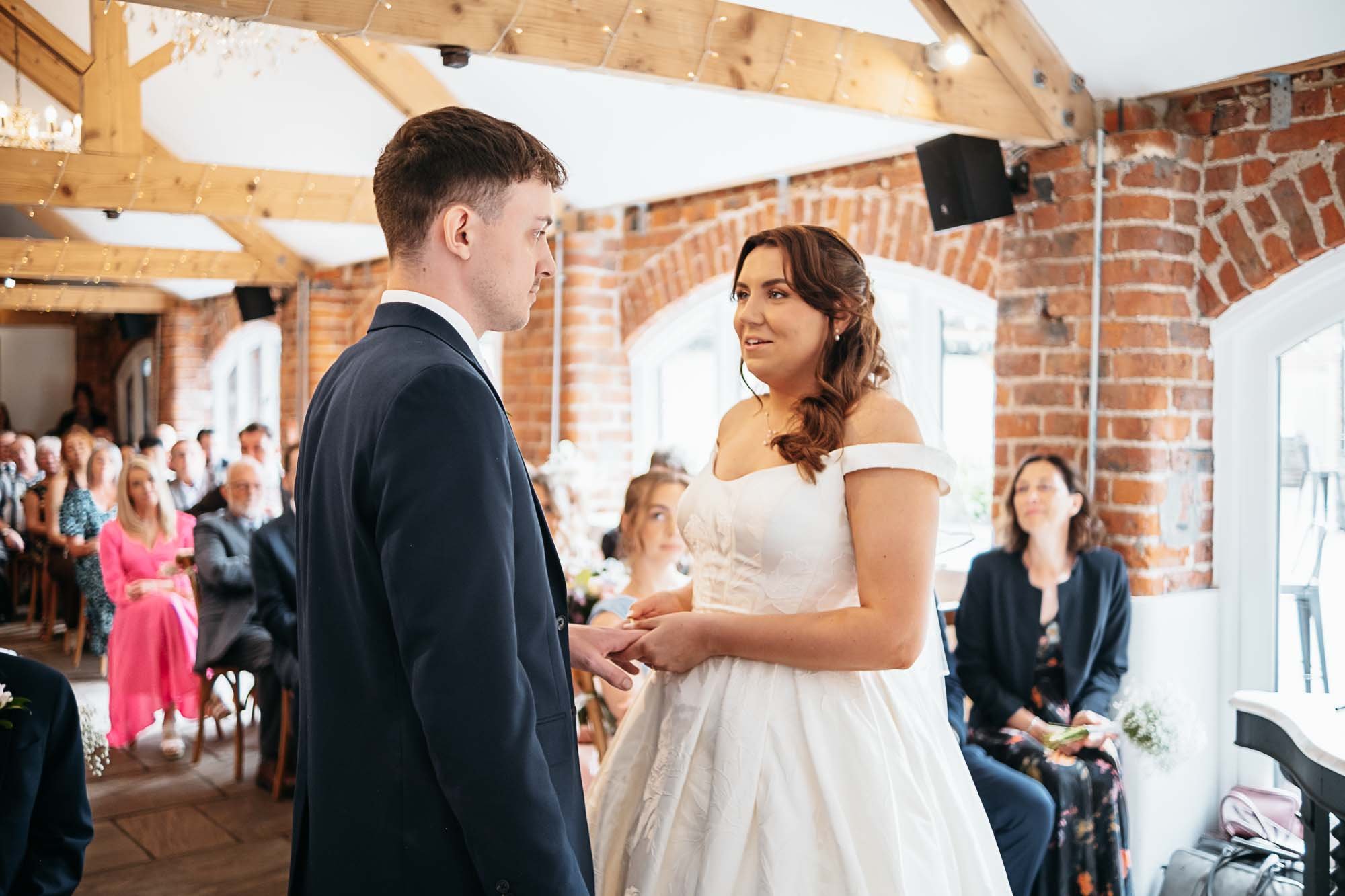 Aimee and Dan facing each other during their ceremony in the oak-beamed barn at Howard Court
