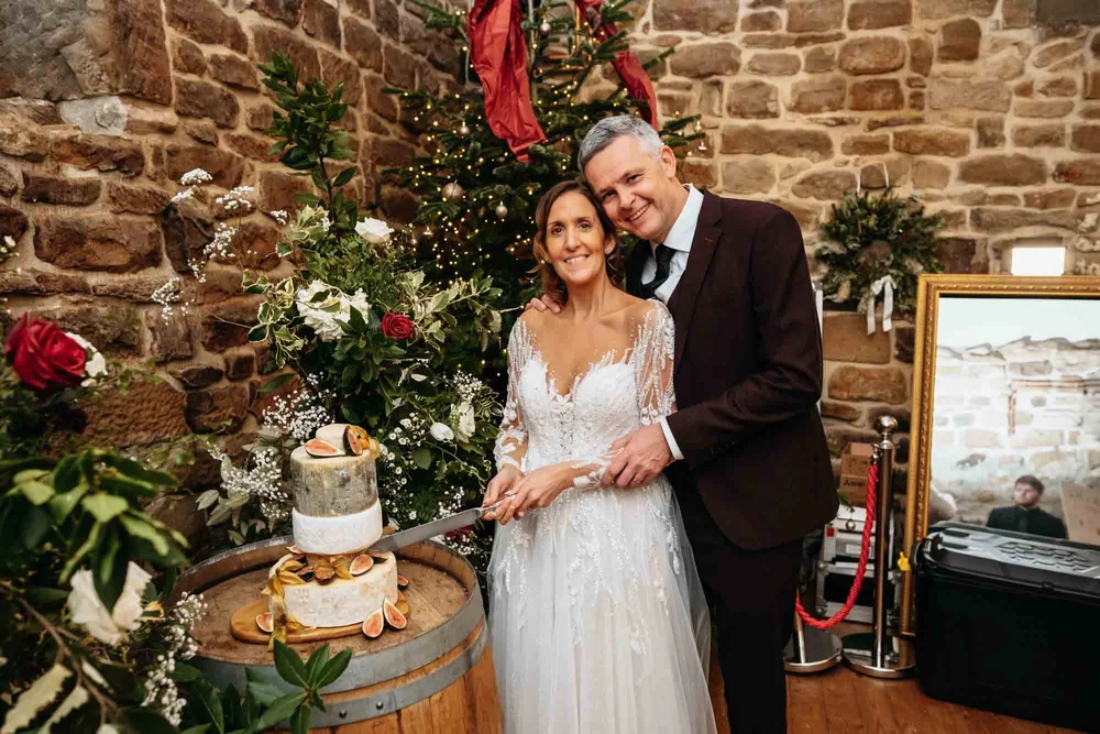 Bride and groom cutting their wedding cake beside the Christmas tree at Danby Castle