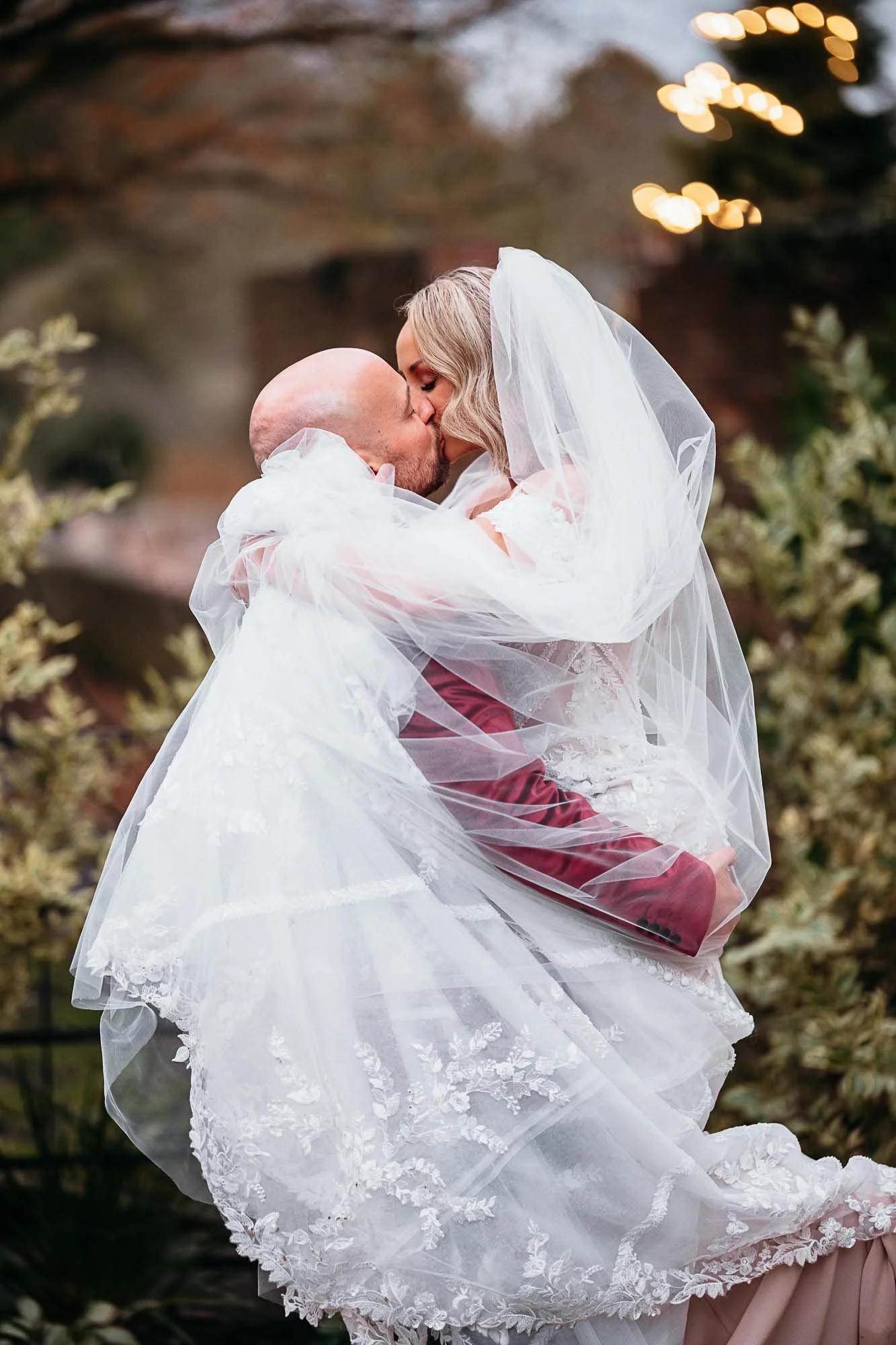 Groom lifting his bride beneath string lights in the gardens at The Croft Hotel
