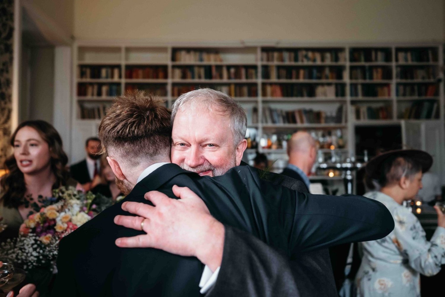Guest hugging the groom in the book-lined room at Middleton Lodge, North Yorkshire