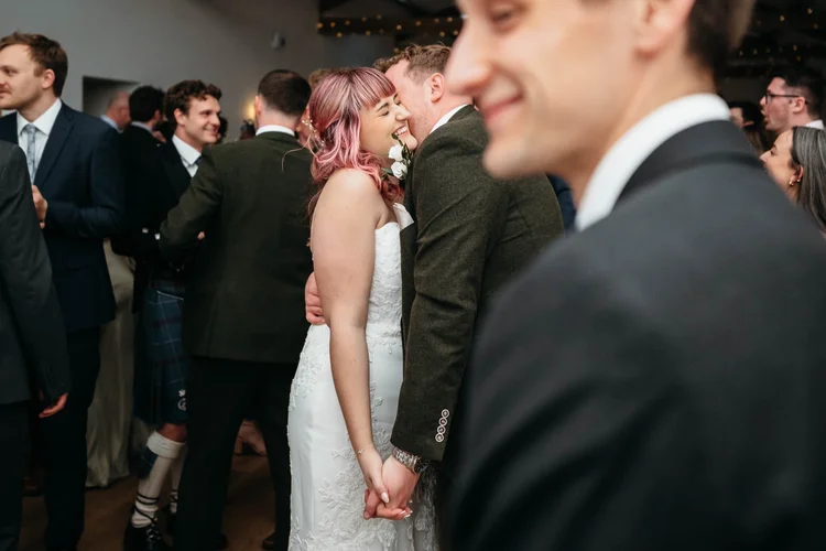 Bride laughing with her husband and wedding guests inside the Old Barn at Danby Castle
