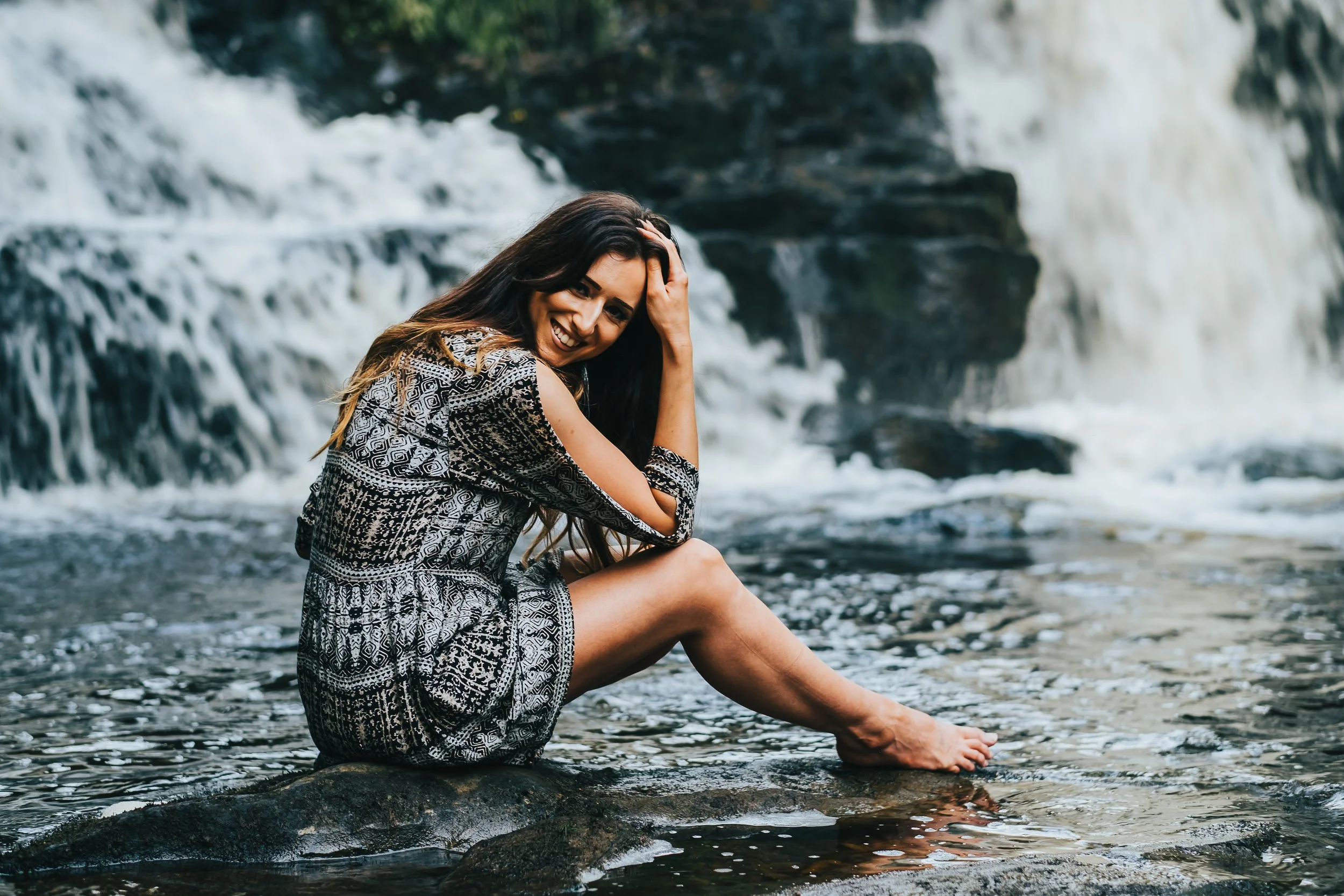 women sits near waterfall and looks into the camera smiling
