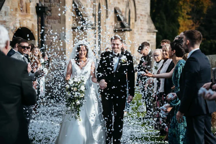 A newly married couple laughing as their guests shower them in confetti