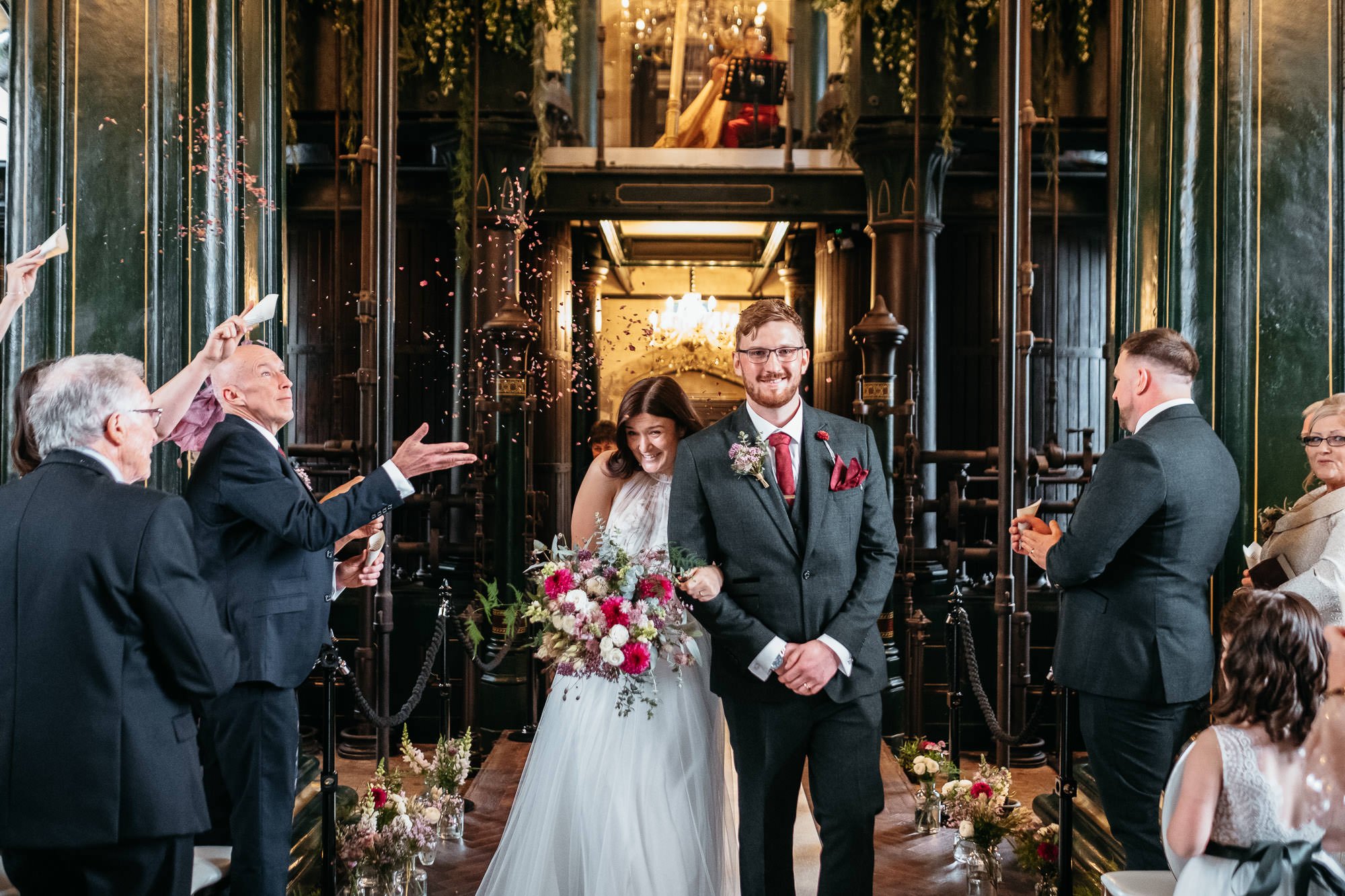 A wedding ceremony with a bride and groom walking down the aisle, surrounded by guests celebrating with confetti in a grand, vintage-style hall.