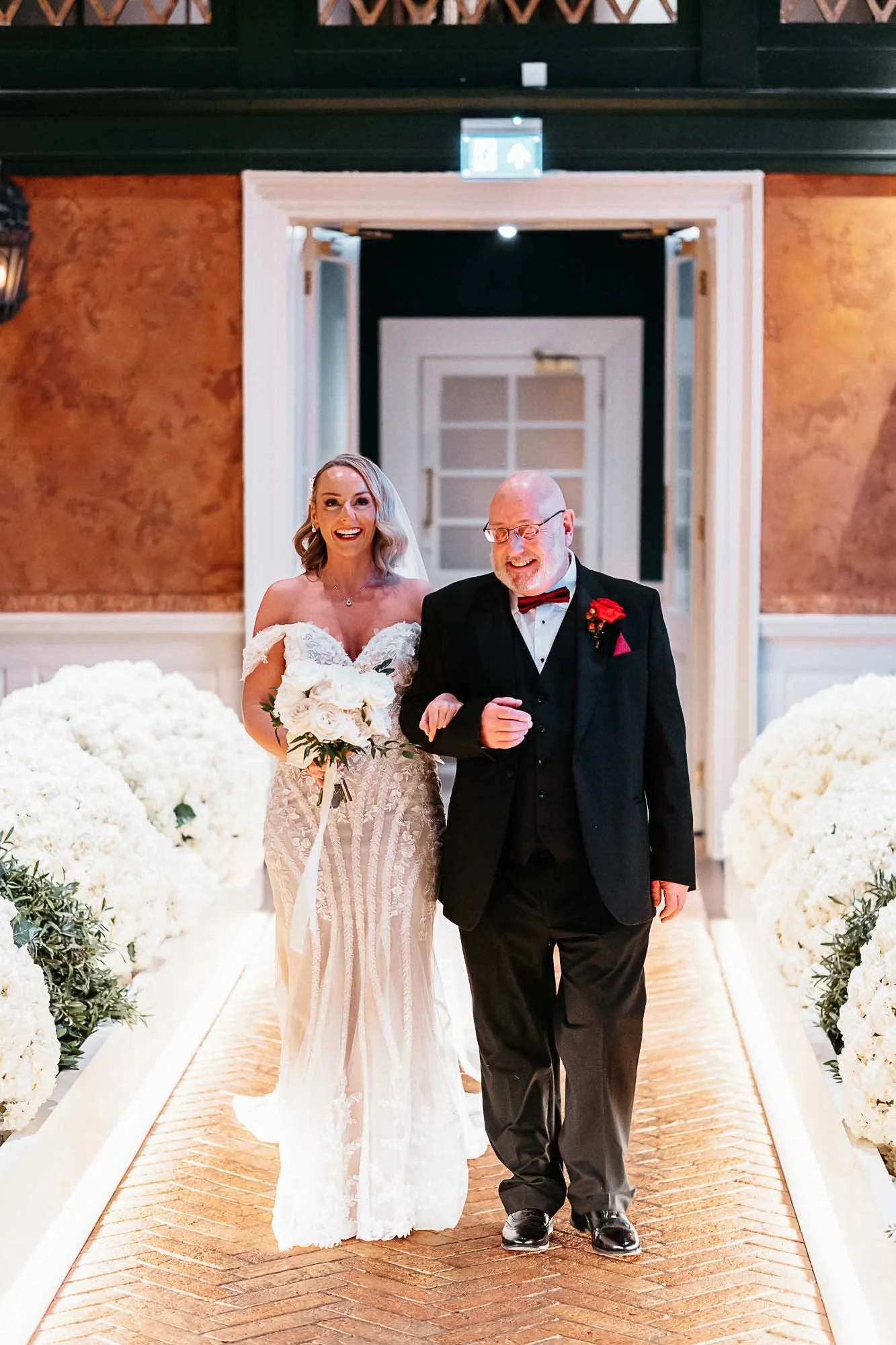 Bride and her father walking the runway aisle at The Croft Hotel lined with white florals