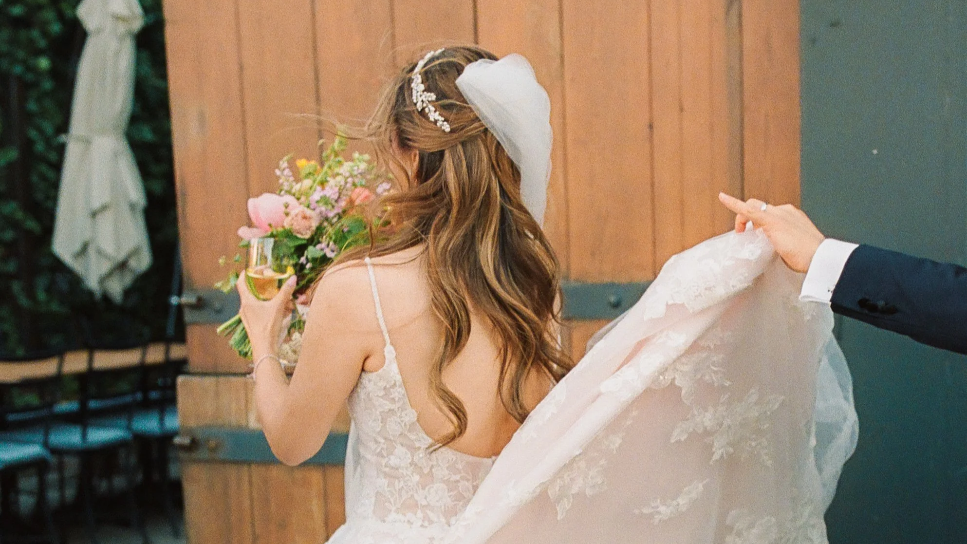 A bride holding a bouquet of flowers while a person, possibly the groom, lifts the hem of her wedding dress.