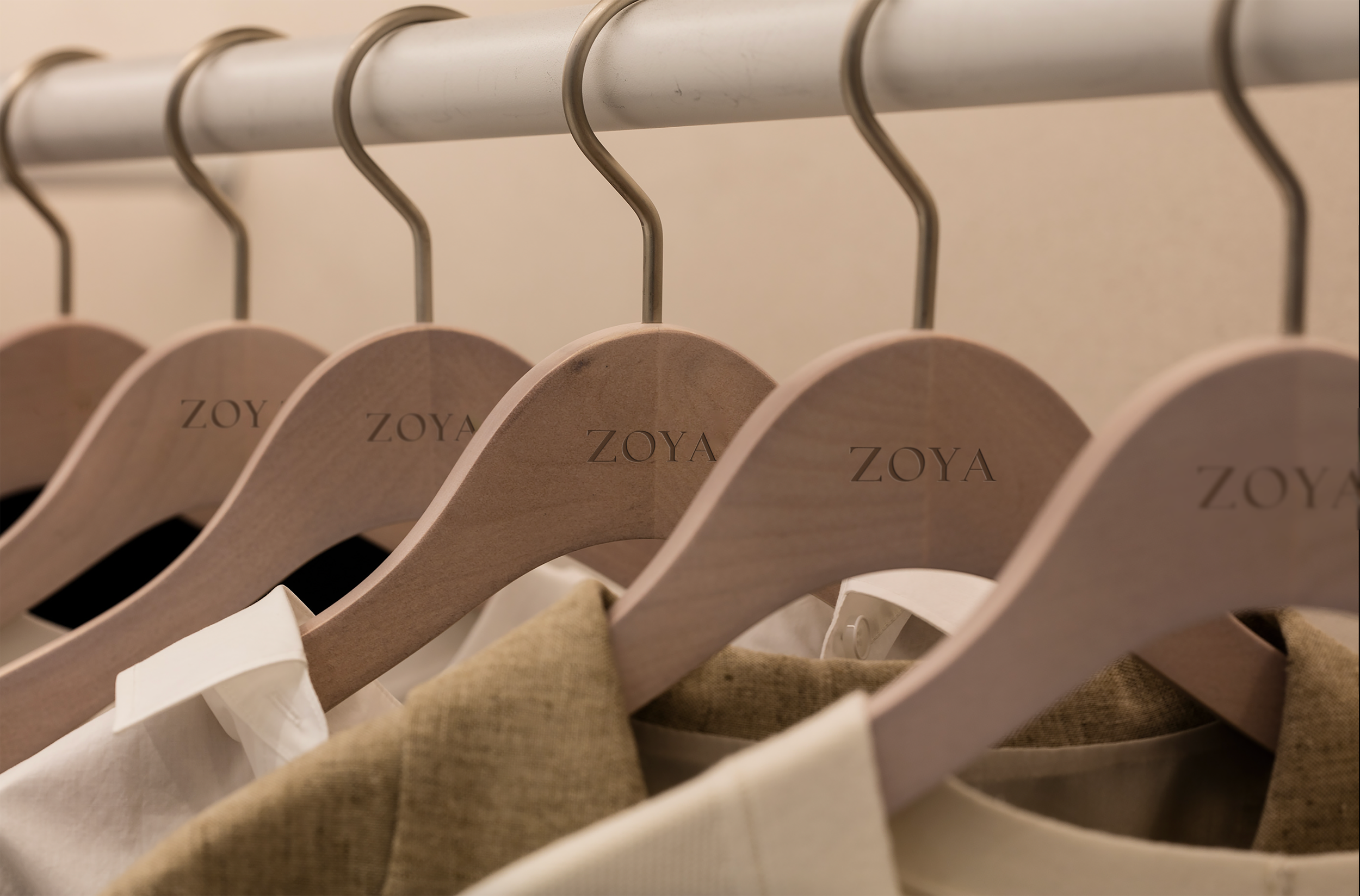 Several beige clothing hangers on a metal rod, each with the brand name 'ZOYA' engraved, holding various clothing items.