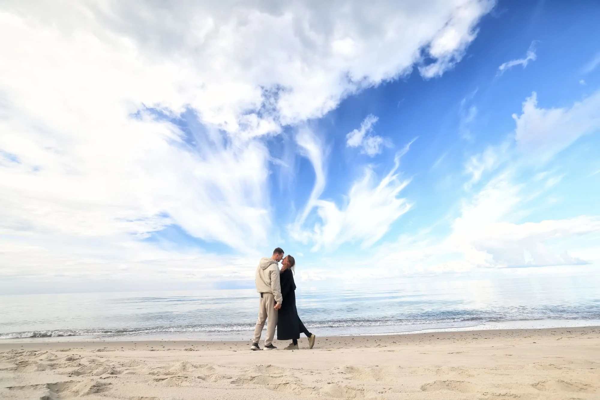 A young couple kiss during a winters walk by the sea. It looks cold but bright