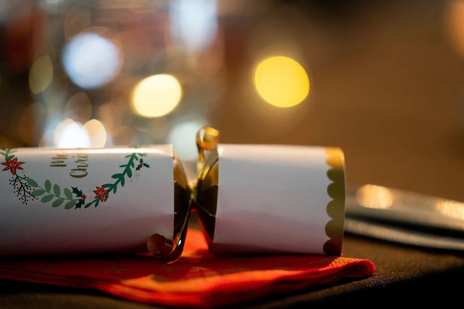 A Christmas cracker close up with cutlery and festive lighting blurred in the background