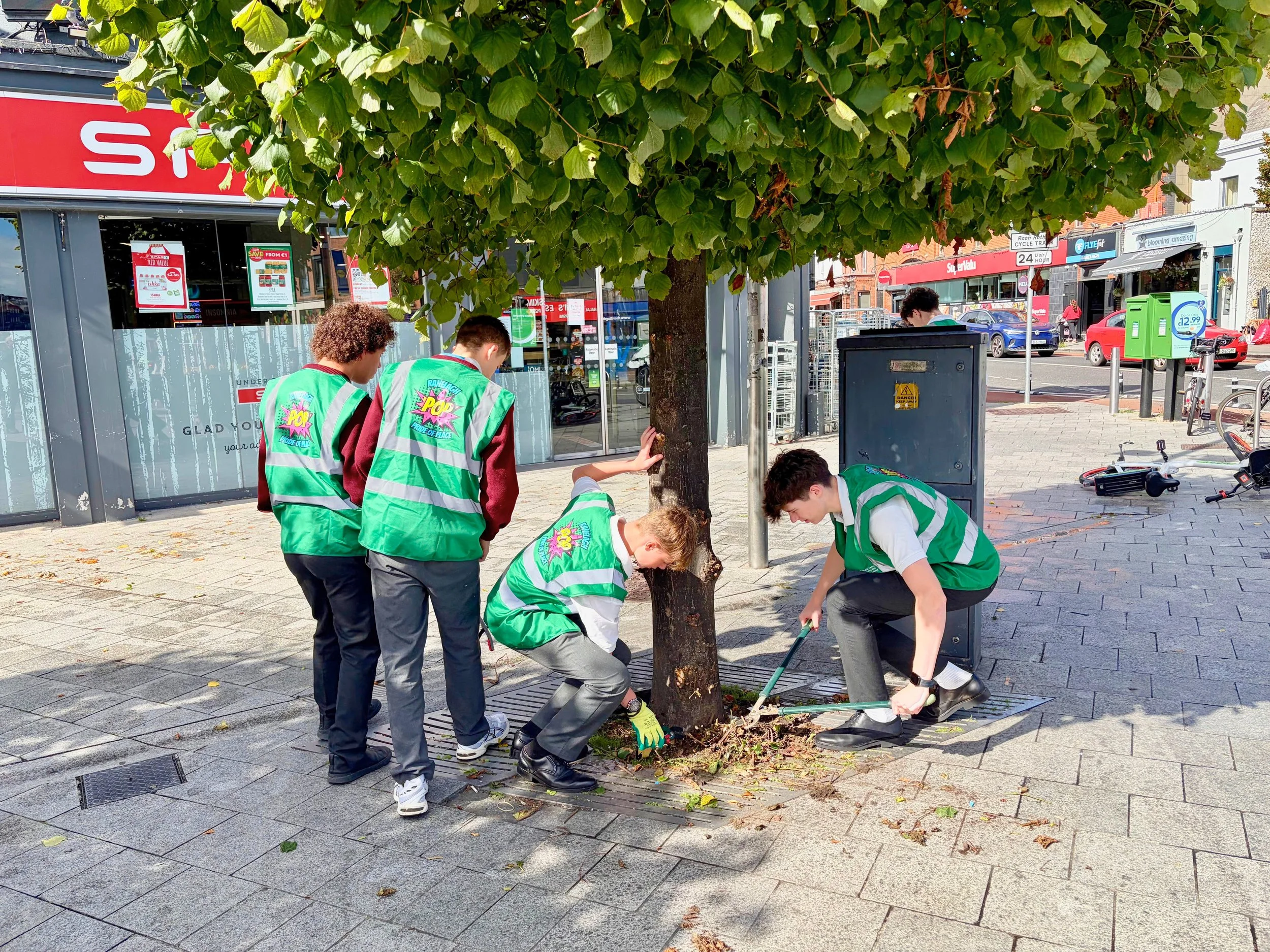 Volunteers in high visibility vests tidying a street tree outside a local shop in the community